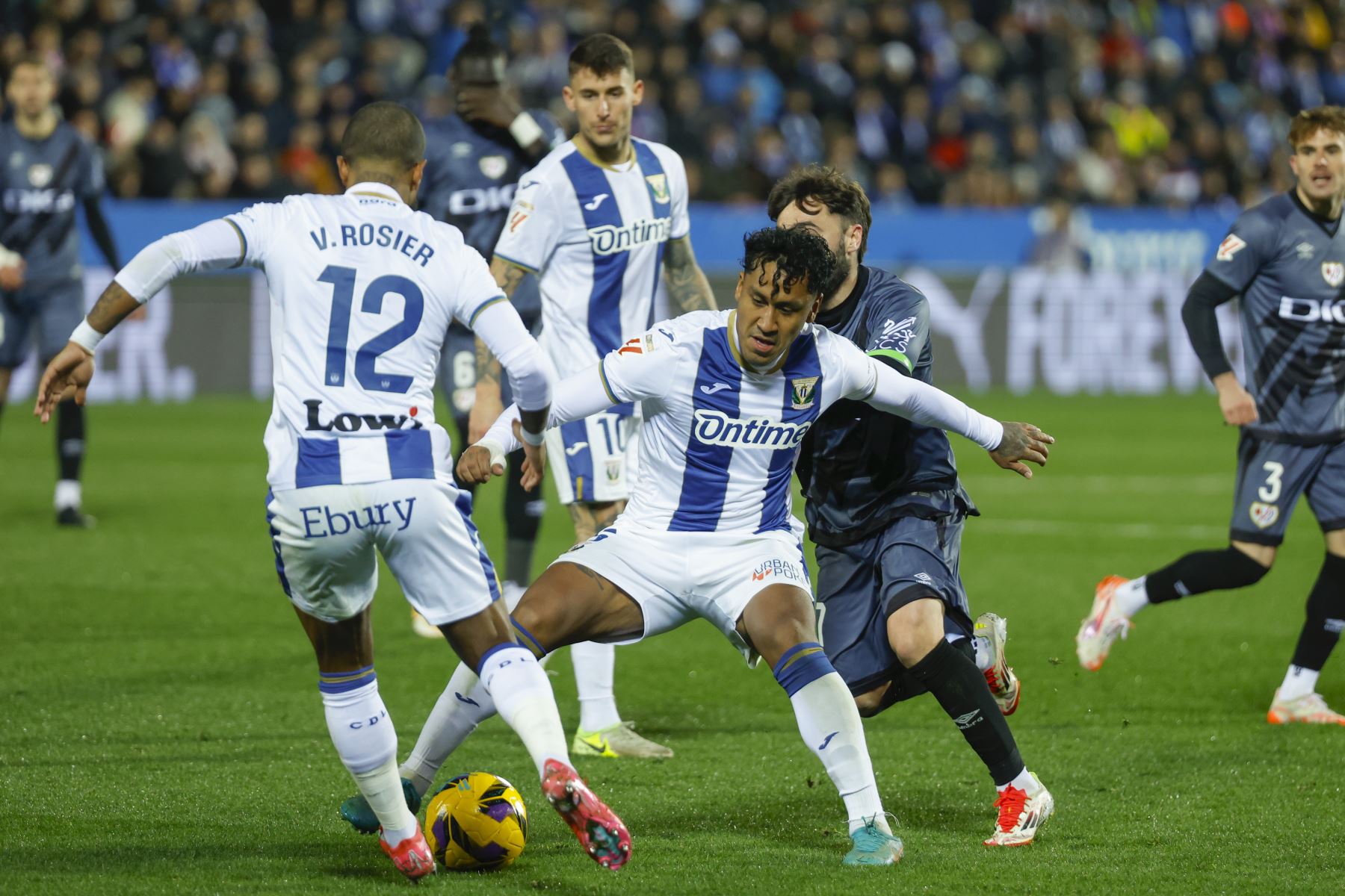 El defensa francés del Leganés Valentin Rosier (i) saca el balón ante la presión del Rayo con ayuda de su compañero Renato Tapia durante el encuentro correspondiente a la jornada 22 de Laliga EA Sports que disputan hoy viernes Leganés y Rayo Vallecano en el estadio de Butarque, en la localidad madrileña. Foto: EFE