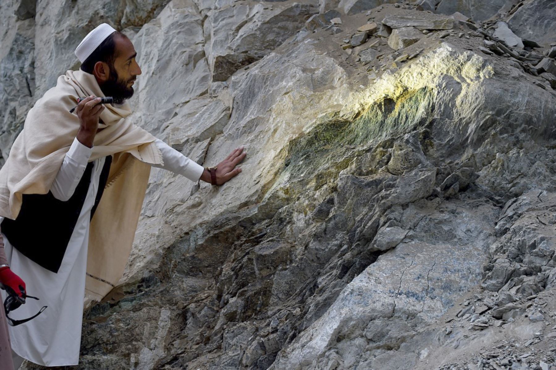 Un minero afgano usa una linterna para inspeccionar una roca, en una mina de nefrita en las montañas del distrito de Goshta, provincia de Nangarhar. El gobierno talibán quiere atraer inversionistas locales y extranjeros con la riqueza subterránea del país para asegurar una fuente de ingresos cruciales. Bajo el paisaje rocoso de Afganistán hay esmeraldas, rubíes, mármol, oro y litio valorados en billones de dólares, según estudios de Estados Unidos y la ONU de 2010 y 2013. Foto: AFP