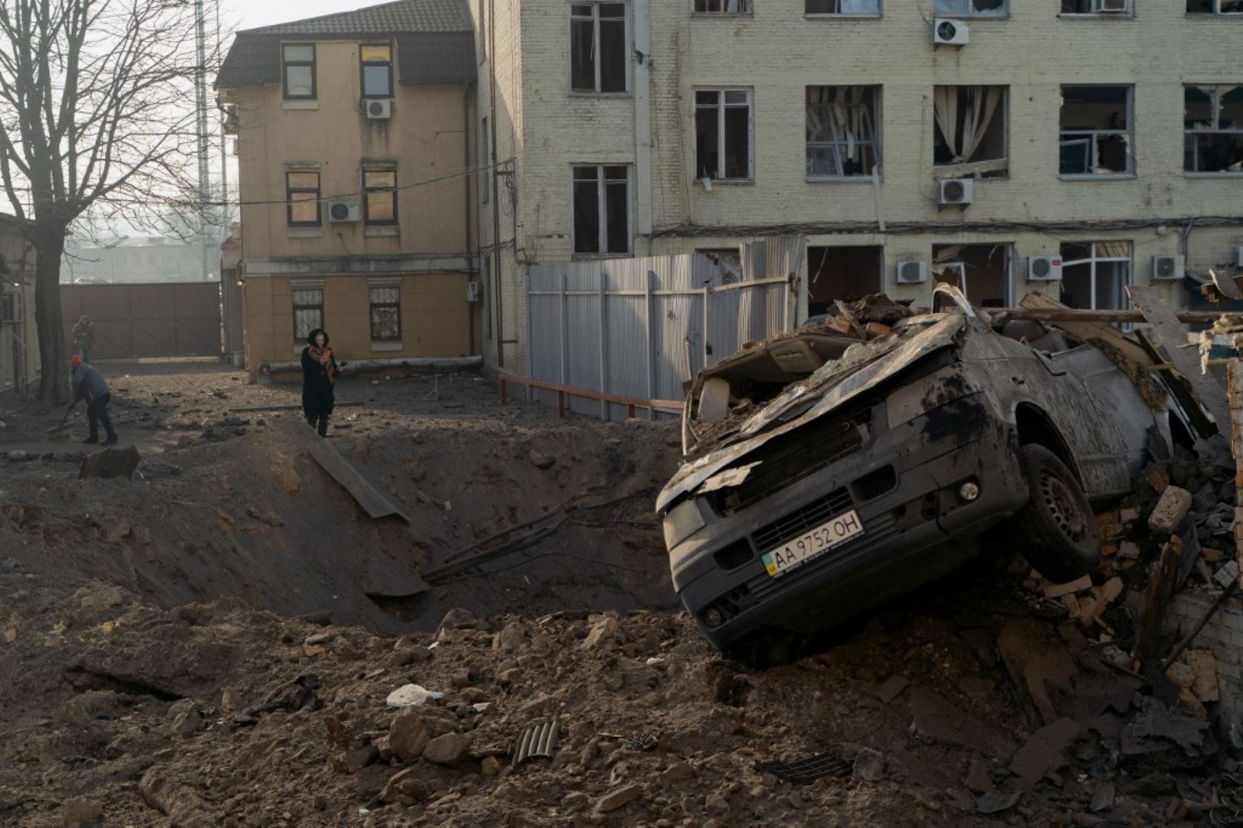 Una mujer está de pie junto a un cráter y un vehículo destruido después de un ataque con misiles en Kiev el 12 de febrero de 2025, en medio de la invasión rusa de Ucrania. (Foto de Tetiana DZHAFAROVA / AFP)