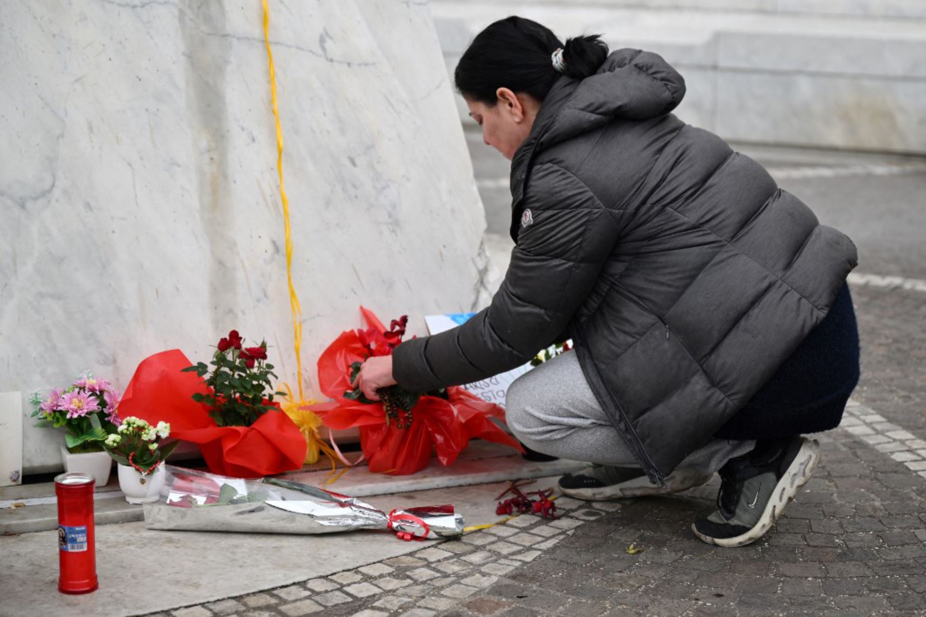 Una mujer lleva flores a la estatua de Juan Pablo II afuera del hospital Gemelli, donde está internado el Papa Francisco, en Roma, el 24 de febrero de 2025. Foto: AFP