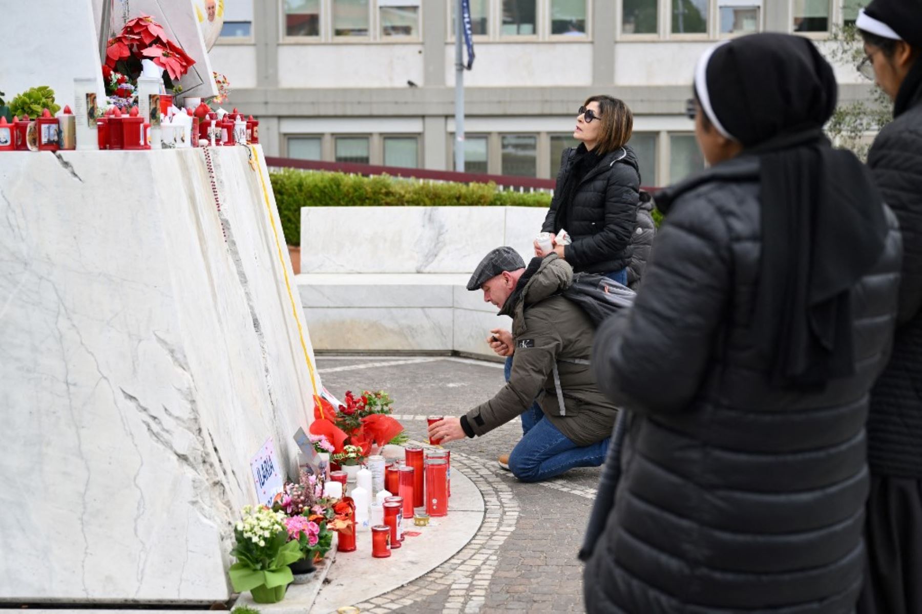 Un hombre lleva flores a la estatua de Juan Pablo II afuera del hospital Gemelli, donde está internado el Papa Francisco, en Roma, el 24 de febrero de 2025. Foto: AFP