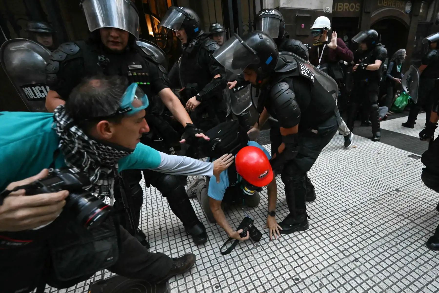 Policías antidisturbios se enfrentan a fotoperiodistas durante una protesta de jubilados apoyados por aficionados al fútbol contra el gobierno del presidente Javier Milei en Buenos Aires. AFP