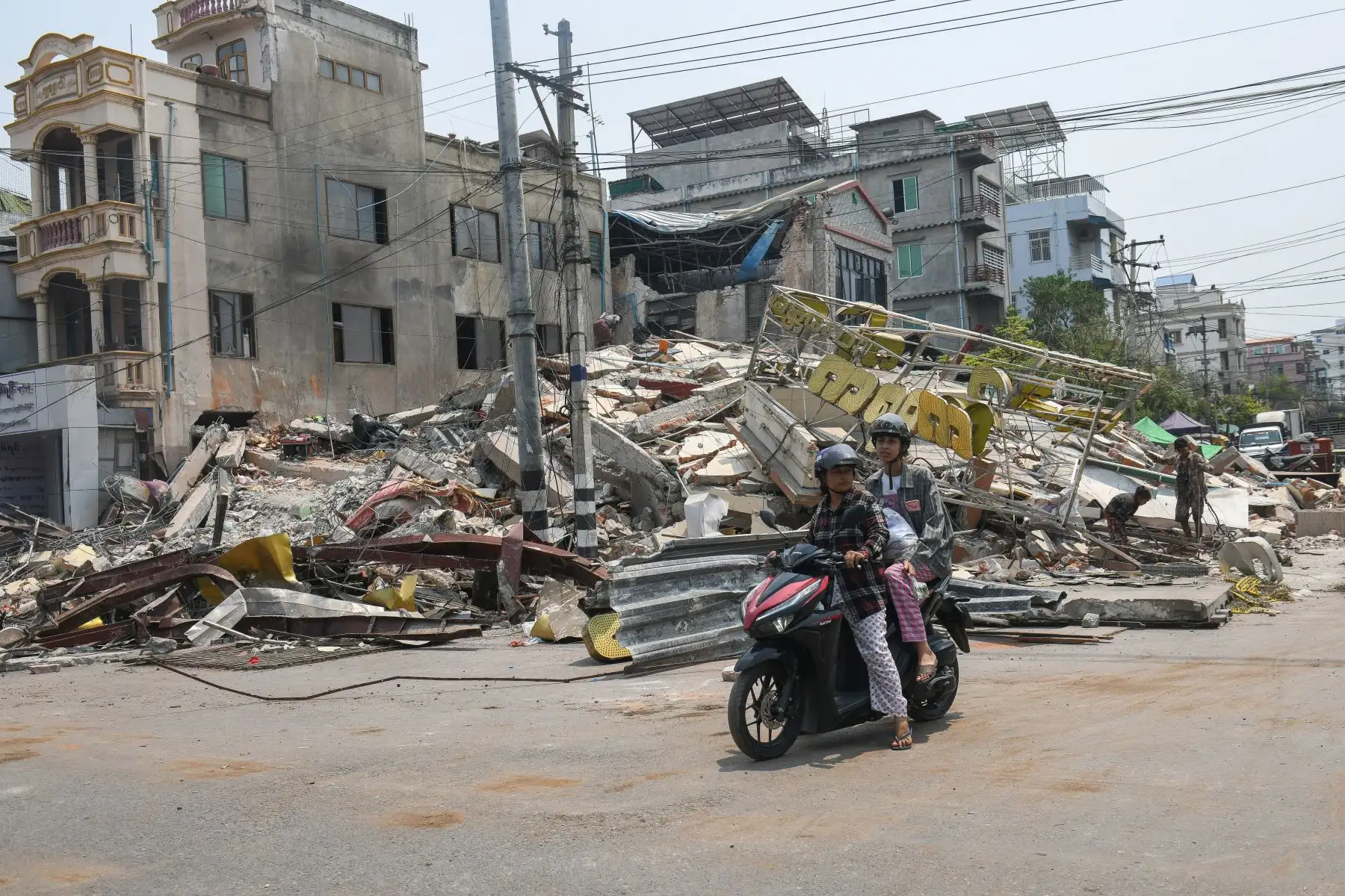 La gente viaja en motocicleta frente a edificios dañados en Mandalay.
Foto: AFP