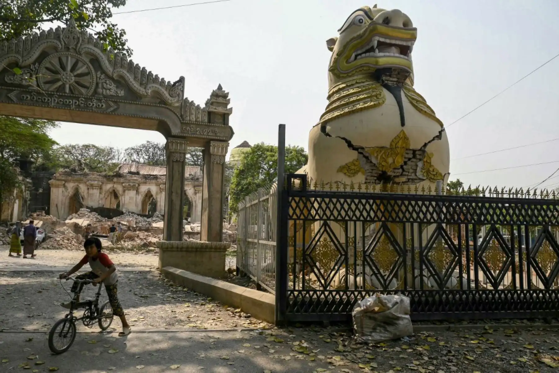 Un niño juega en bicicleta junto a una estatua de león budista agrietada en las afueras de Mandalay el 2 de abril de 2025, cinco días después de que un gran terremoto azotara el centro de Myanmar. Foto: AFP