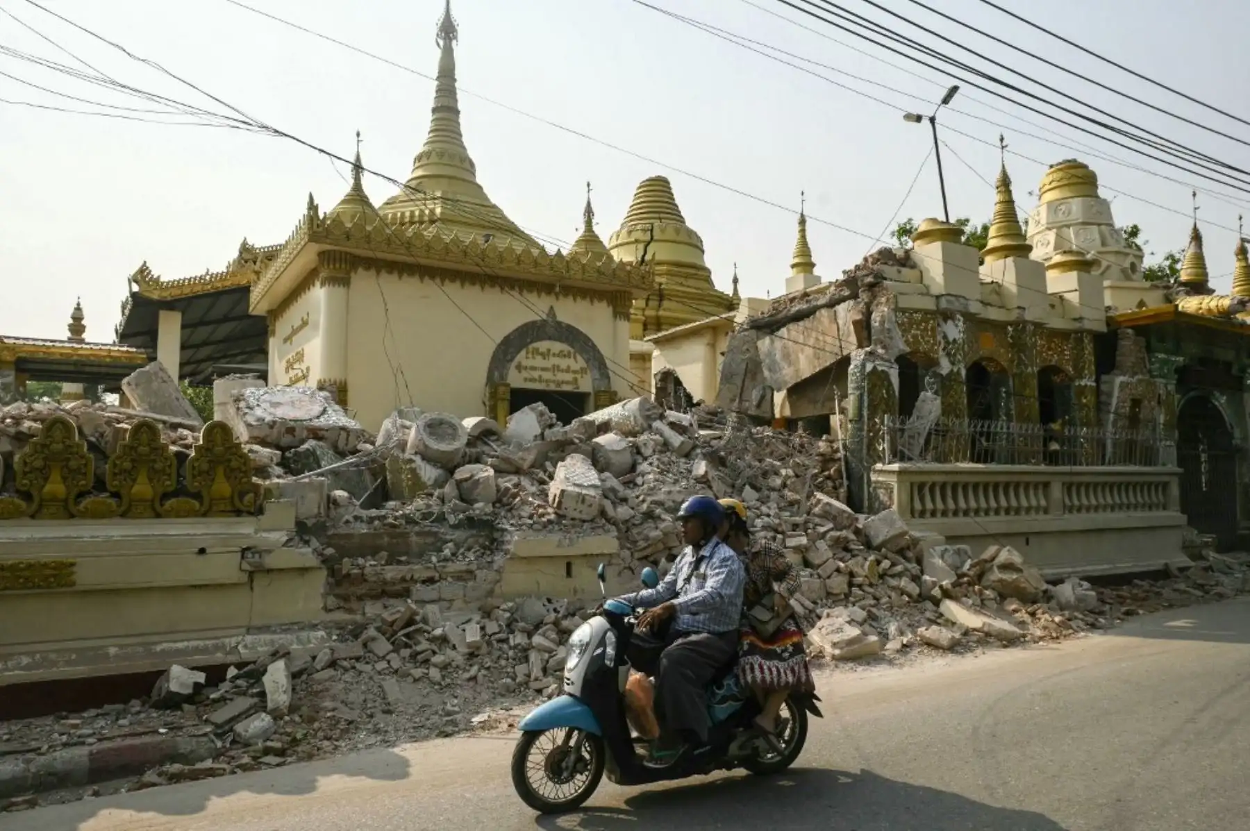Personas en moto pasan junto a los escombros de una pagoda budista dañada en Mandalay. Foto. AFP