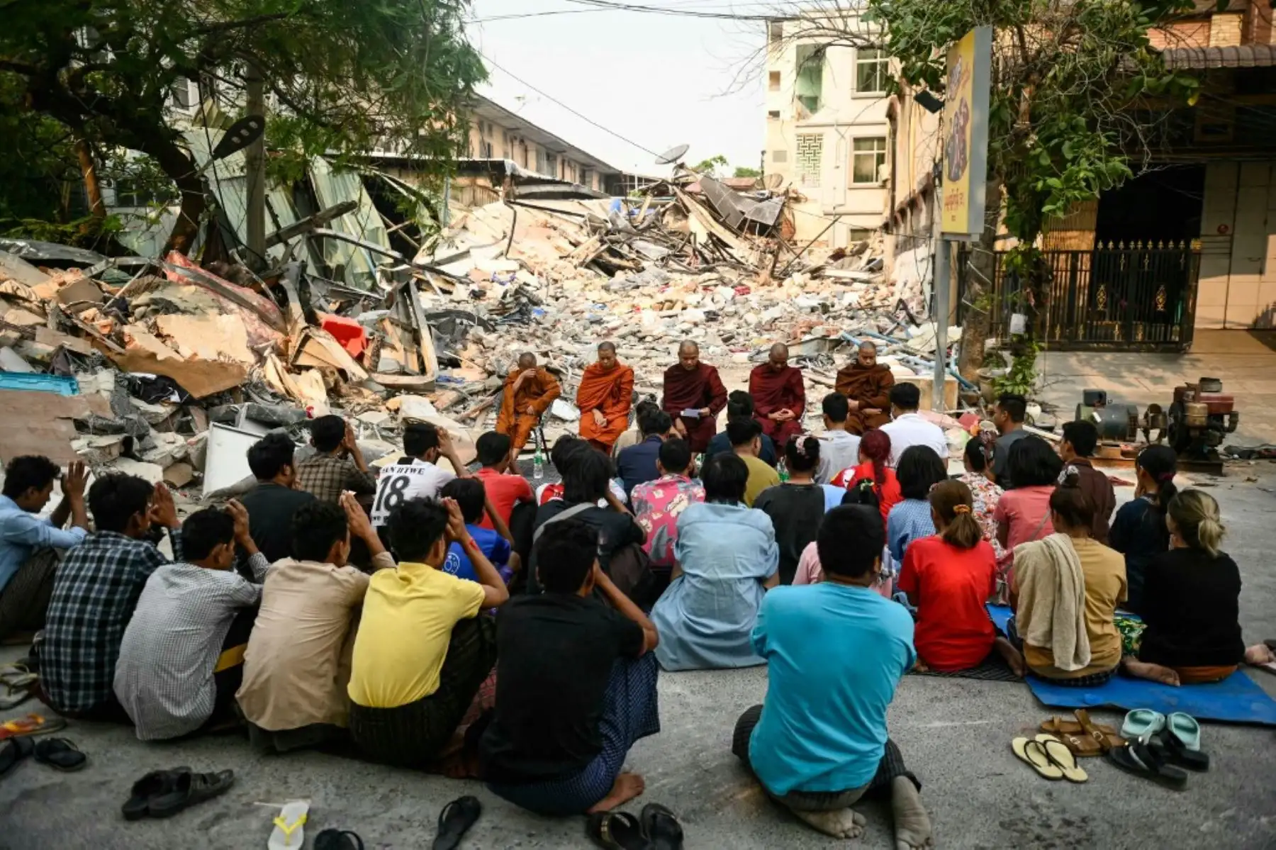 Personas asisten a un servicio conmemorativo budista en el suelo, junto a los escombros de un edificio derrumbado en Mandalay, el 3 de abril de 2025, tras el terremoto del 28 de marzo que azotó el centro de Myanmar. Foto: AFP
