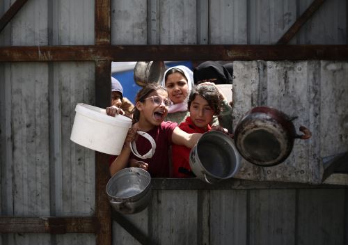 Niños palestinos hacen un gesto mientras hacen fila para recoger una comida en un punto de distribución de alimentos gratuitos en el campo de refugiados de Nuseirat, en el centro de Gaza. Foto: AFP/Archivo