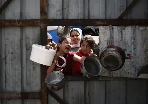 Niños palestinos hacen un gesto mientras hacen fila para recoger una comida en un punto de distribución de alimentos gratuitos en el campo de refugiados de Nuseirat, en el centro de Gaza. Foto: AFP/Archivo