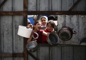 Niños palestinos hacen un gesto mientras hacen fila para recoger una comida en un punto de distribución de alimentos gratuitos en el campo de refugiados de Nuseirat, en el centro de Gaza. Foto: AFP/Archivo