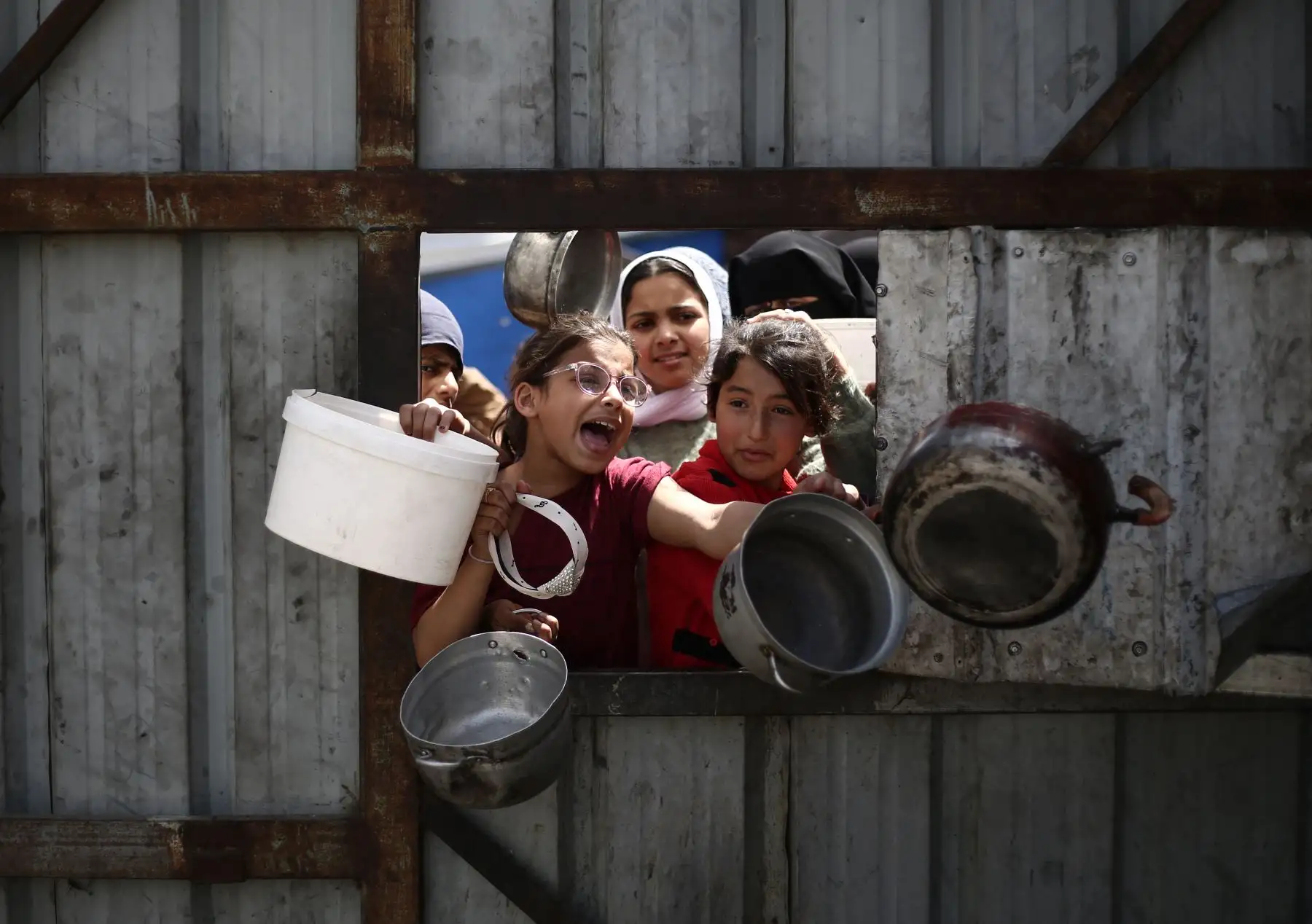 Niños palestinos hacen un gesto mientras hacen fila para recoger una comida en un punto de distribución de alimentos gratuitos en el campo de refugiados de Nuseirat, en el centro de Gaza. Foto: AFP/Archivo