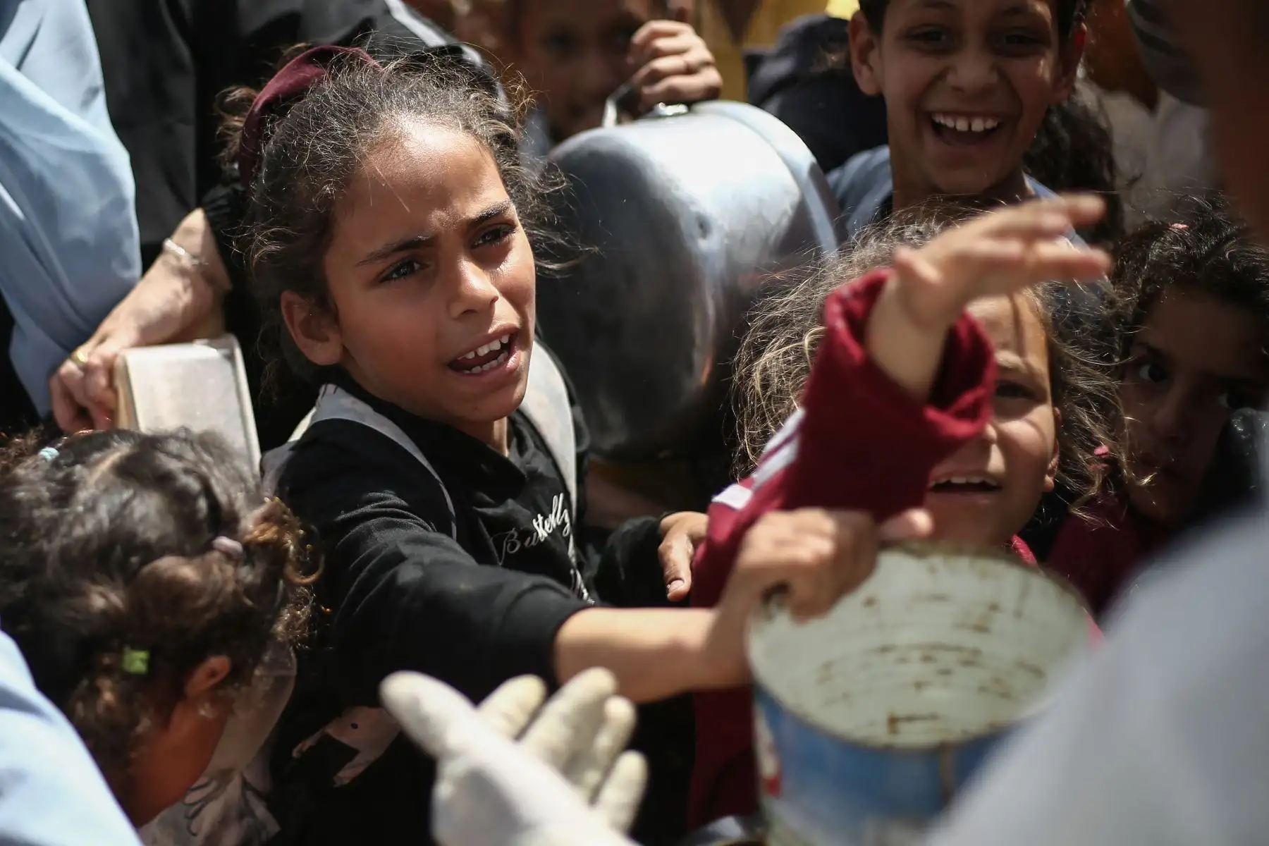 Niños palestinos hacen un gesto mientras hacen fila para recoger una comida en un punto de distribución de alimentos gratuitos en el campo de refugiados de Nuseirat, en el centro de la Franja de Gaza. AFP