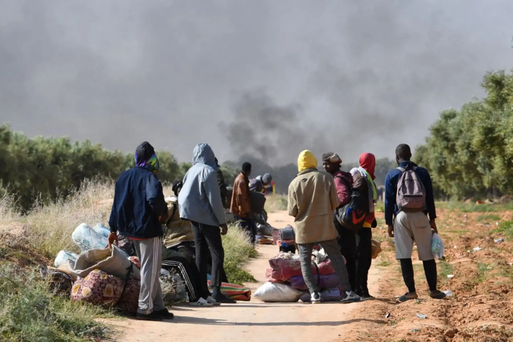 Migrantes salen con sus pertenencias de un campamento para migrantes indocumentados del África subsahariana en Al-Amra, a las afueras de la ciudad portuaria tunecina de Sfax, el 5 de abril de 2025, después de que las autoridades comenzaran a desmantelar el campamento. Túnez desmanteló el viernes campamentos que albergaban a miles de migrantes indocumentados del África subsahariana. Foto: AFP
