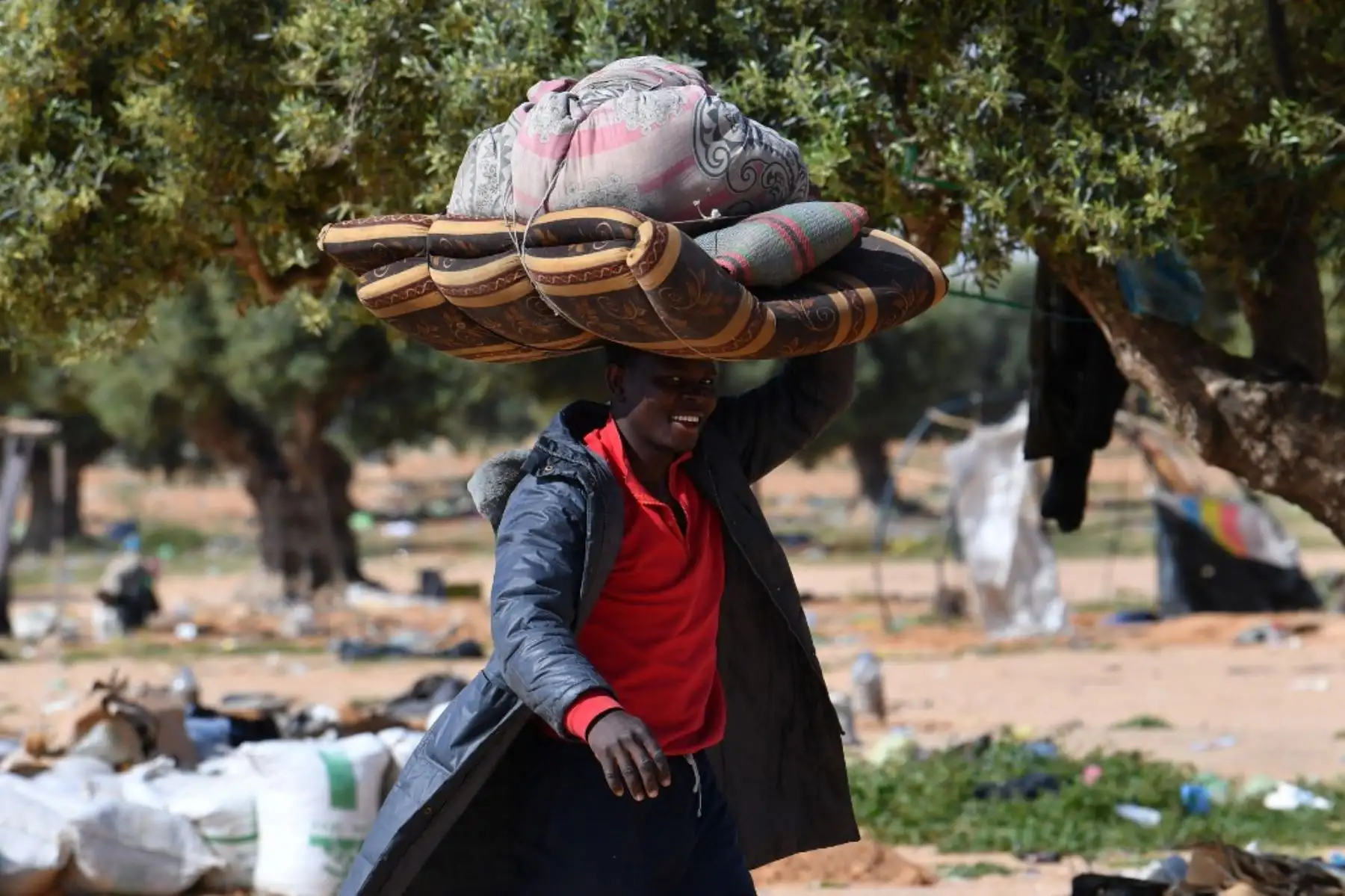 Un migrante carga con sus pertenencias al salir de un campamento para migrantes indocumentados en Al-Amra, a las afueras de la ciudad portuaria tunecina de Sfax, el 5 de abril de 2025, después de que las autoridades comenzaran a desmantelar el campamento. Túnez desmanteló el viernes campamentos que albergaban a miles de migrantes indocumentados del África subsahariana. Foto: AFP