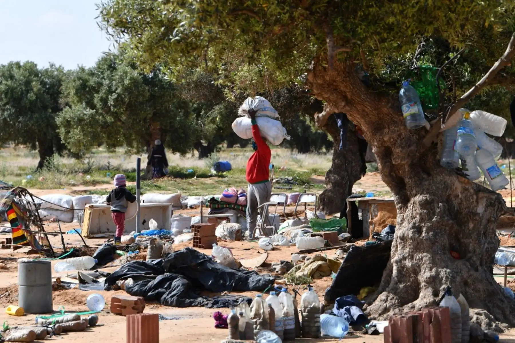 Migrantes recogen sus pertenencias al salir de un campamento para migrantes indocumentados en Al-Amra, a las afueras de la ciudad portuaria tunecina de Sfax, el 5 de abril de 2025, después de que las autoridades comenzaran a desmantelar el campamento. Túnez desmanteló el viernes campamentos que albergaban a miles de migrantes indocumentados del África subsahariana. Foto: AFP
