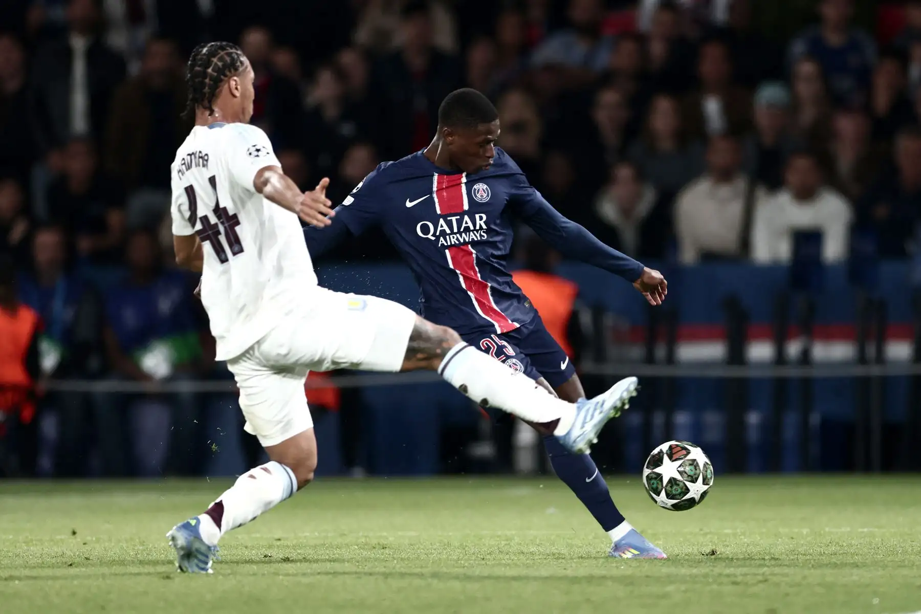 El defensa portugués  del Paris Saint-Germain, Nuno Mendes , cruza el balón frente al centrocampista francés  del Aston Villa, Boubacar Kamara , durante el partido de ida de los cuartos de final de la UEFA Champions League entre el Paris Saint-Germain  y el Aston Villa. AFP