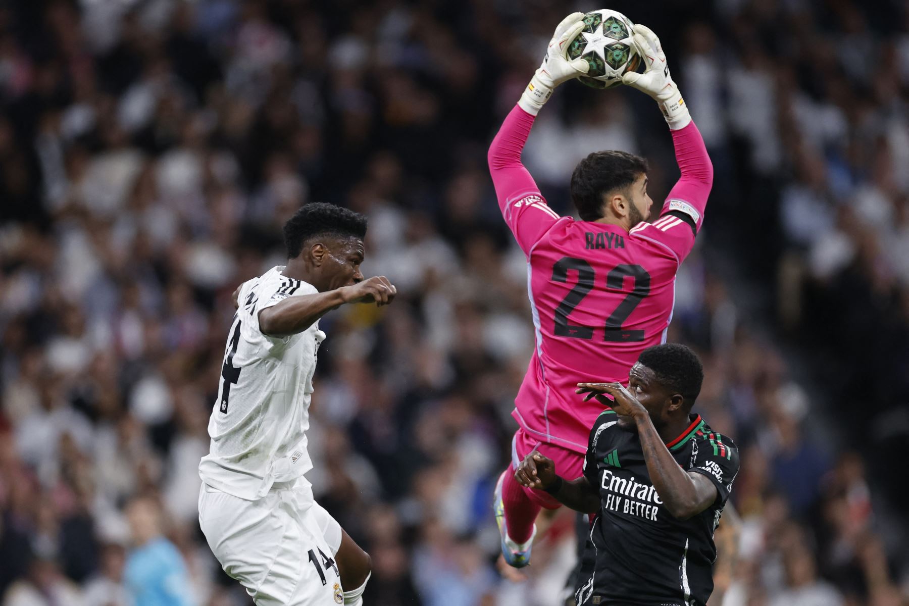 El portero español del Arsenal, David Raya, hace una parada junto al centrocampista francés  del Real Madrid Aurelien Tchouameni y el centrocampista ghanés  del Arsenal, Thomas Partey (R), durante el partido de vuelta de los cuartos de final de la UEFA Champions League entre el Real Madrid CF y el Arsenal. AFP