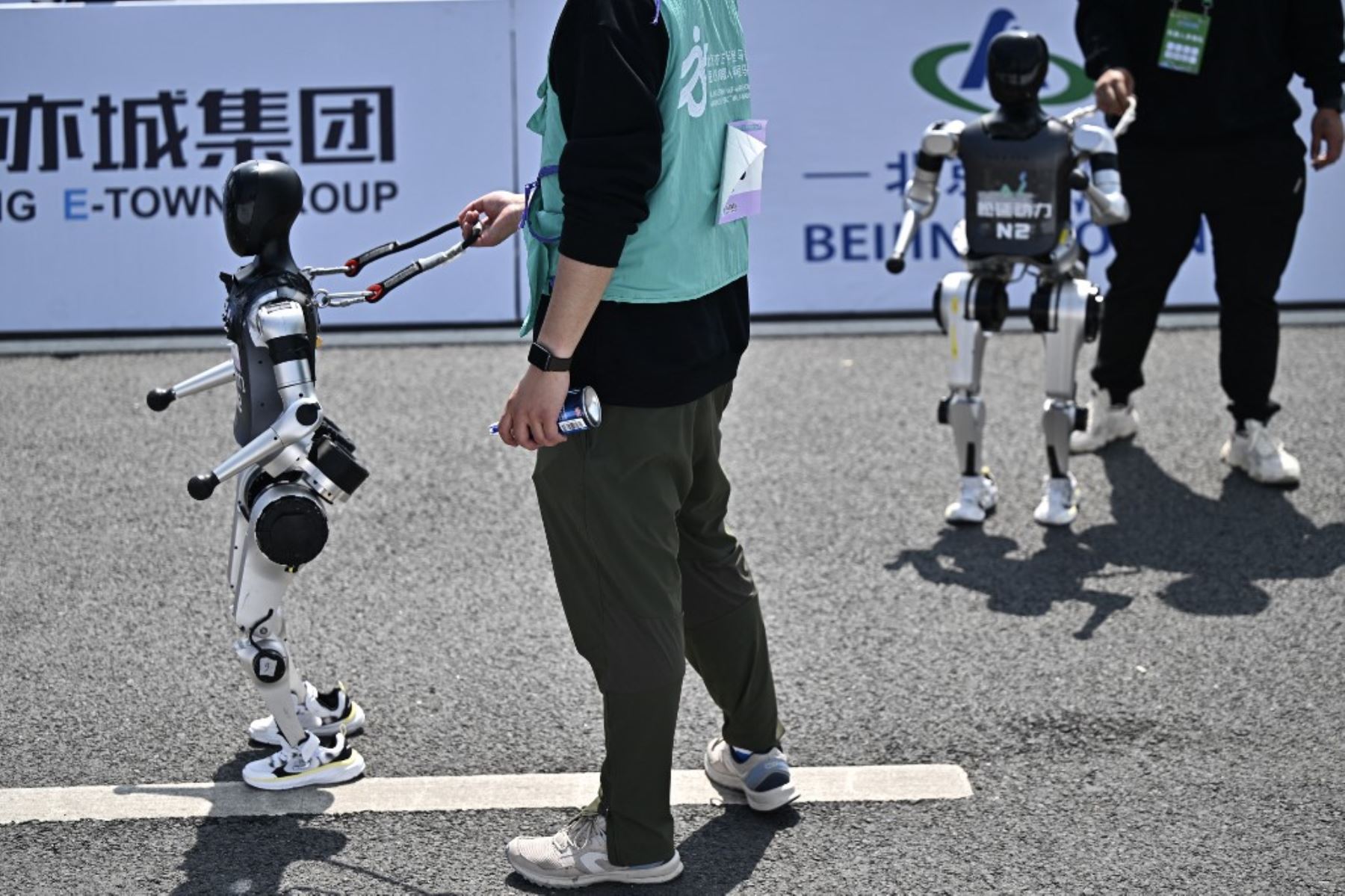 Robots y sus ingenieros después de cruzar la línea de meta en la media maratón de robots humanoides en Beijing el 19 de abril de 2025. Decenas de estos robots salieron a las calles de Beijing, uniéndose a miles de participantes en una media maratón pionera en el mundo que muestra el impulso de China para liderar la carrera mundial en tecnología de vanguardia. Foto: AFP