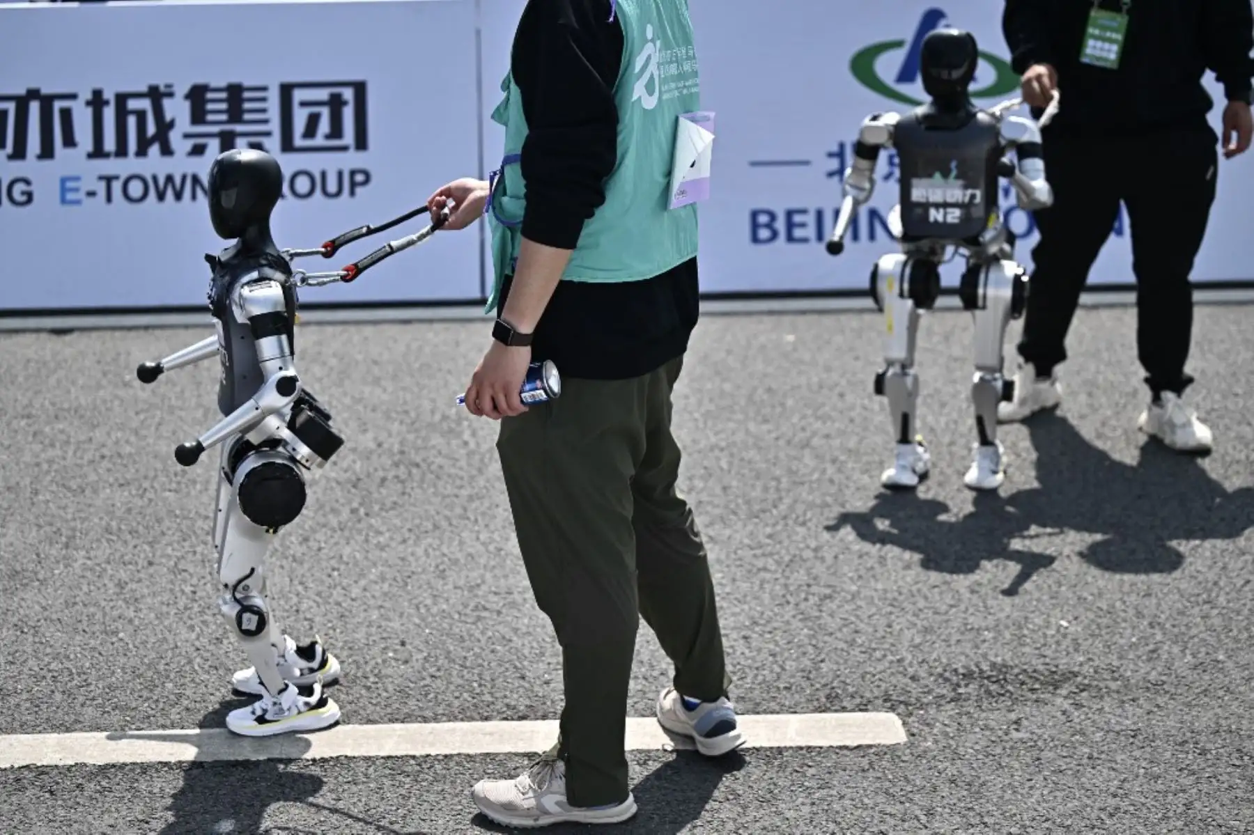 Robots y sus ingenieros después de cruzar la línea de meta en la media maratón de robots humanoides en Beijing el 19 de abril de 2025. Decenas de estos robots salieron a las calles de Beijing, uniéndose a miles de participantes en una media maratón pionera en el mundo que muestra el impulso de China para liderar la carrera mundial en tecnología de vanguardia. Foto: AFP