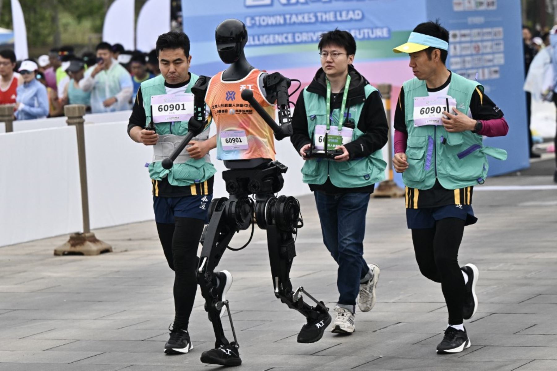 Un robot y sus ingenieros corren en la media maratón de robots humanoides en Beijing el 19 de abril de 2025. Decenas de estos robots salieron a las calles de Beijing, uniéndose a miles de participantes humanos en una media maratón pionera en el mundo que muestra el impulso de China para liderar la carrera mundial en tecnología de vanguardia. Foto: AFP