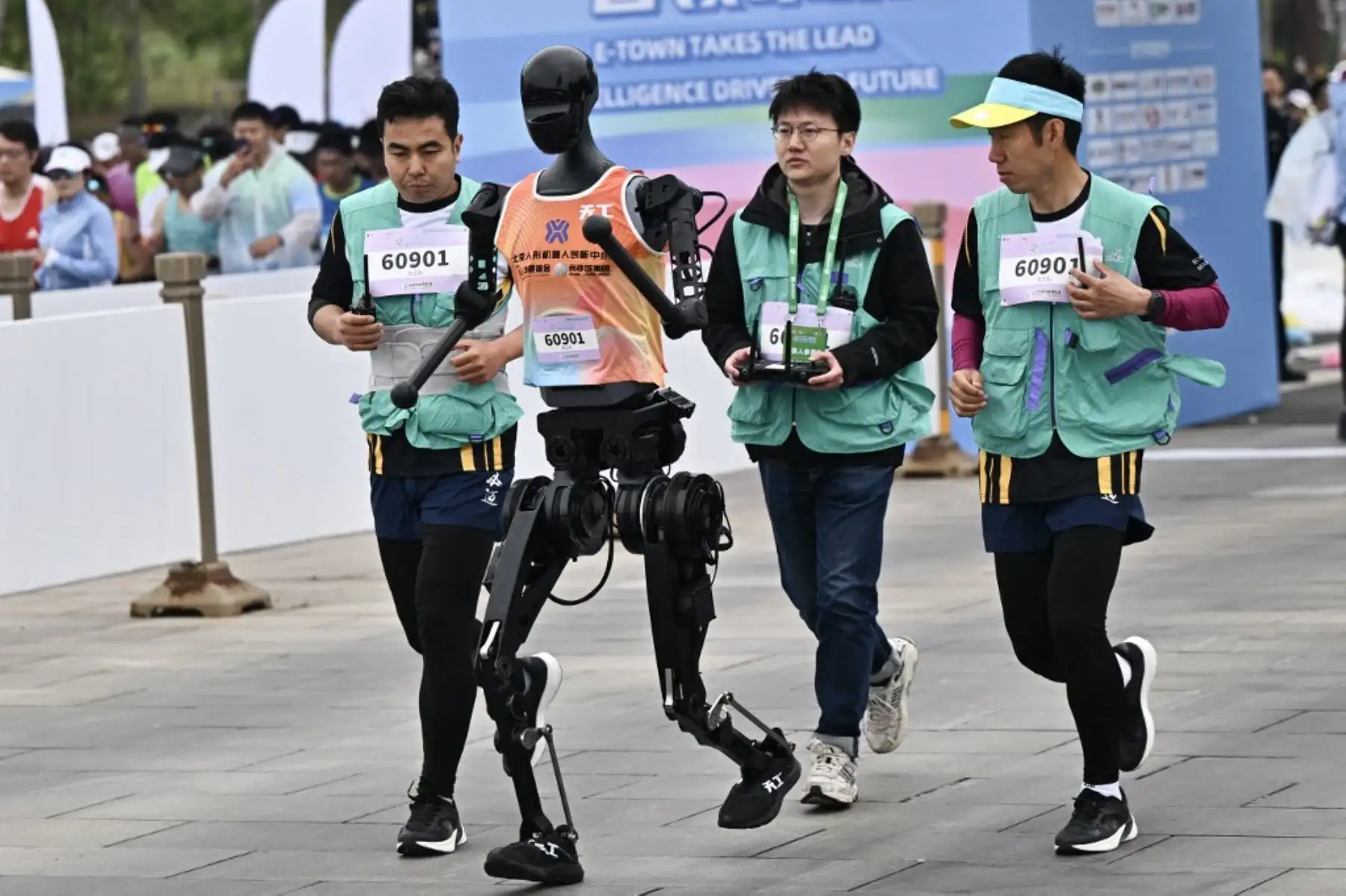 Un robot y sus ingenieros corren en la media maratón de robots humanoides en Beijing el 19 de abril de 2025. Decenas de estos robots salieron a las calles de Beijing, uniéndose a miles de participantes humanos en una media maratón pionera en el mundo que muestra el impulso de China para liderar la carrera mundial en tecnología de vanguardia. Foto: AFP