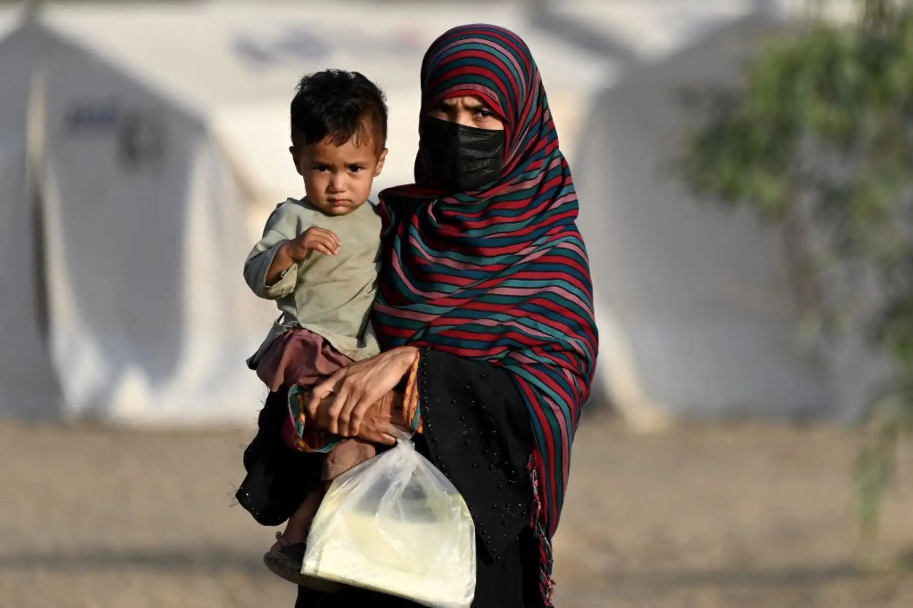 Una mujer refugiada afgana sostiene a un niño mientras llega desde Pakistán a un campamento improvisado cerca de la frontera entre Afganistán y Pakistán en Torkham, en la provincia de Nangarhar, el 20 de abril de 2025. Foto: AFP