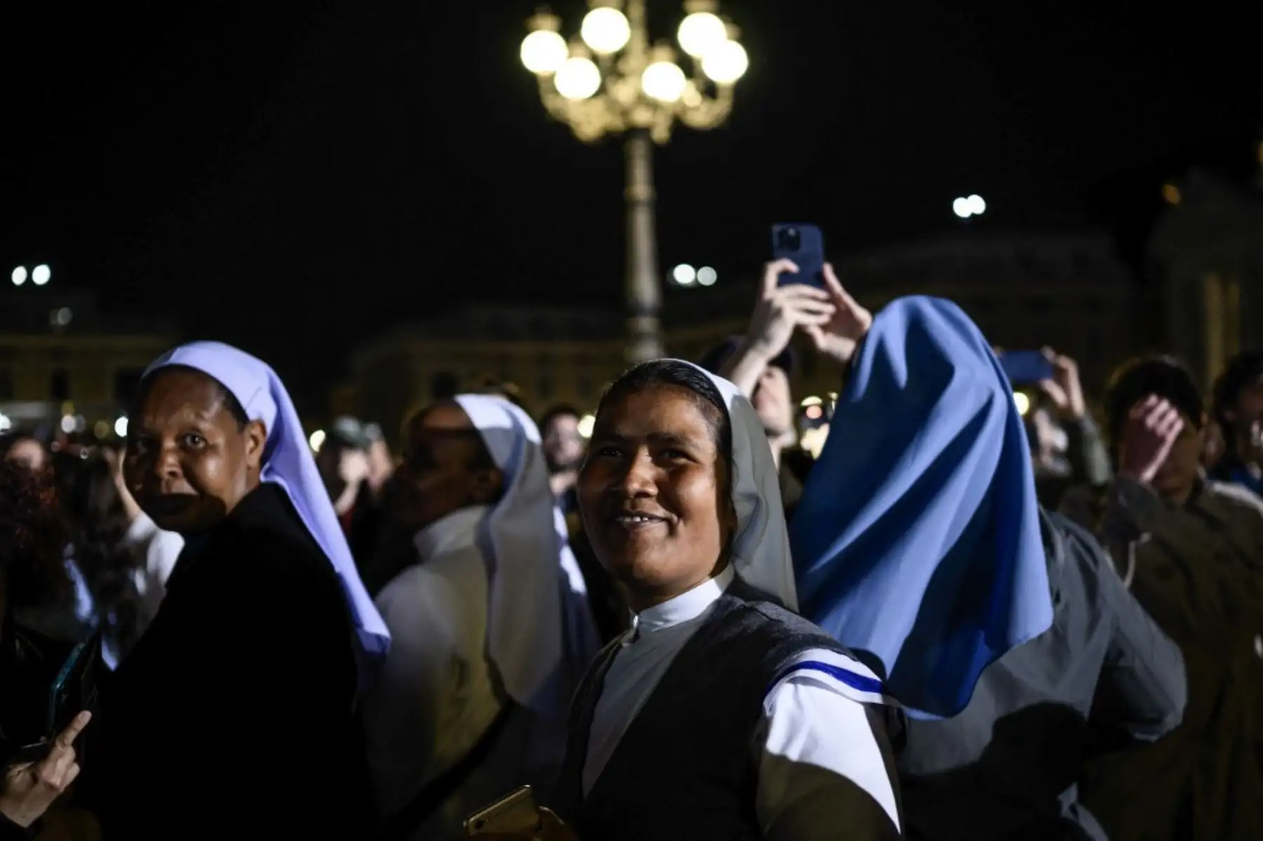 Monjas se encuentran en la Plaza de San Pedro a la expectativa de la elección del nuevo Papa, mientras una columna de humo negro se eleva desde la chimenea de la Capilla Sixtina, lo que indica que los cardenales no lograron elegir un nuevo papa en la segunda vuelta de su cónclave secreto en el Vaticano, el 7 de mayo de 2025. Foto: AFP