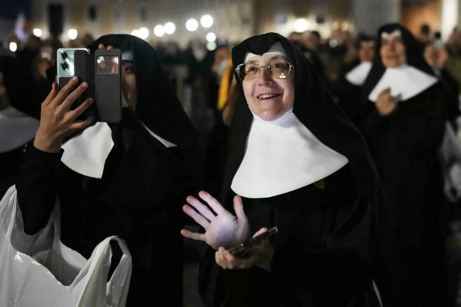 Monjas se encuentran en la Plaza de San Pedro a la expectativa de la elección del nuevo Papa, mientras una columna de humo negro se eleva desde la chimenea de la Capilla Sixtina, lo que indica que los cardenales no lograron elegir un nuevo papa en la segunda vuelta de su cónclave secreto en el Vaticano, el 7 de mayo de 2025. Foto: AFP