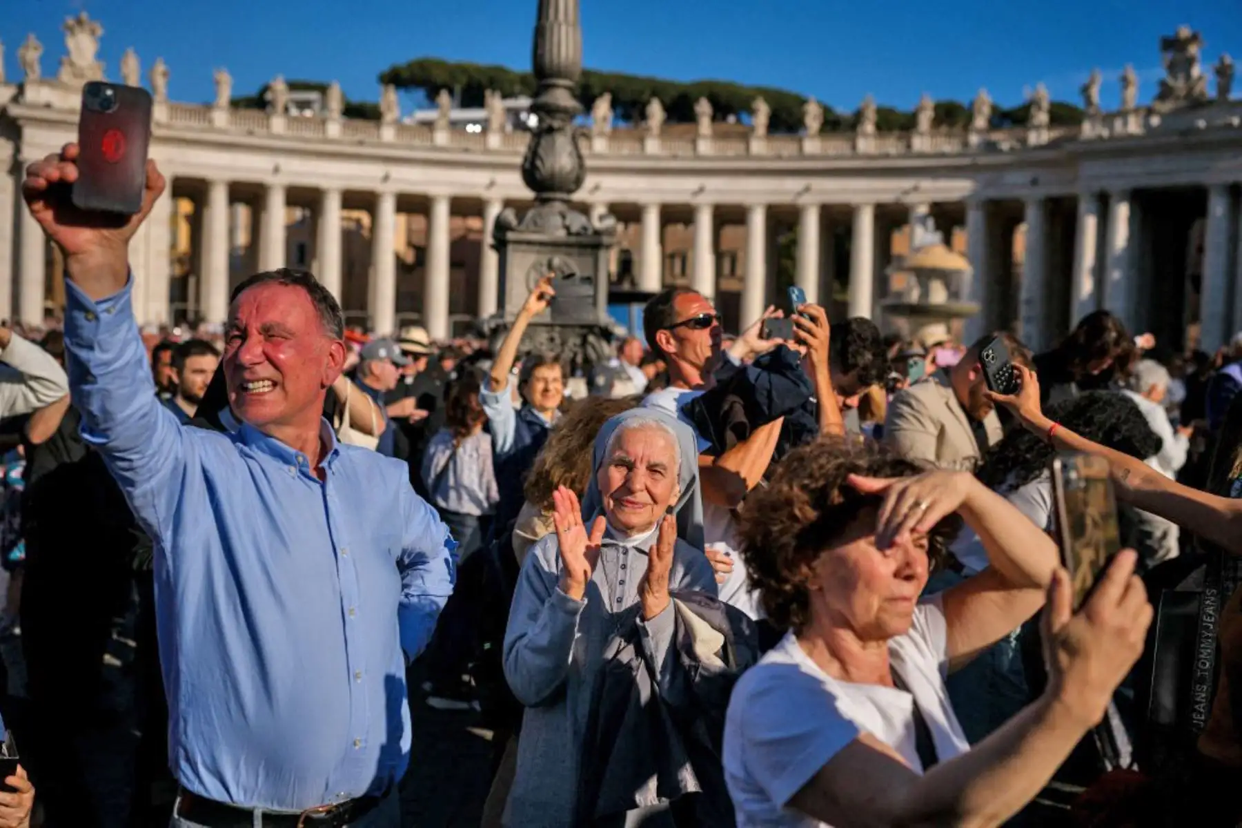 La gente reacciona y ondea banderas del Vaticano mientras una columna de humo blanco, anuncia que los cardenales eligieron un nuevo papa durante su cónclave en el Vaticano el 8 de mayo de 2025. Foto: AFP