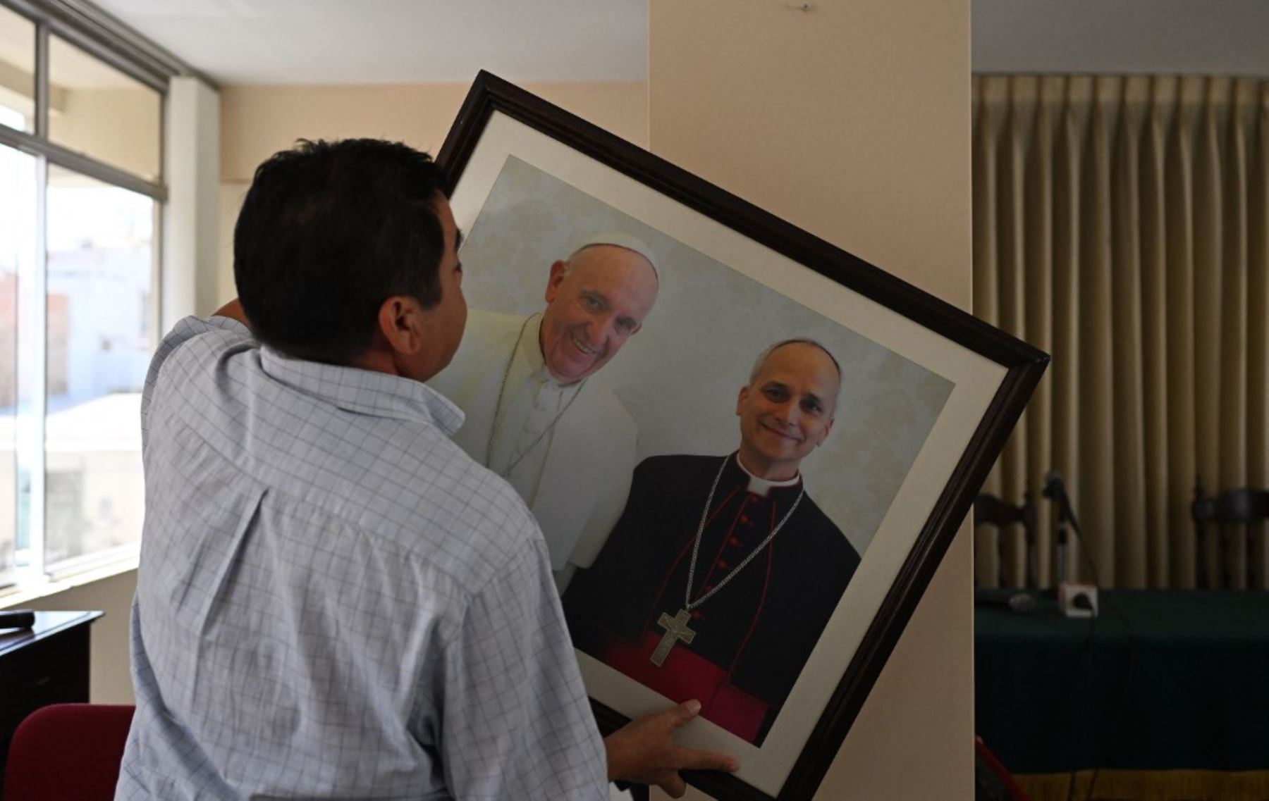 Un hombre cuelga una imagen del difunto papa Francisco y del papa León XIV antes de una conferencia de prensa en el palacio episcopal de Chiclayo. Foto: AFP