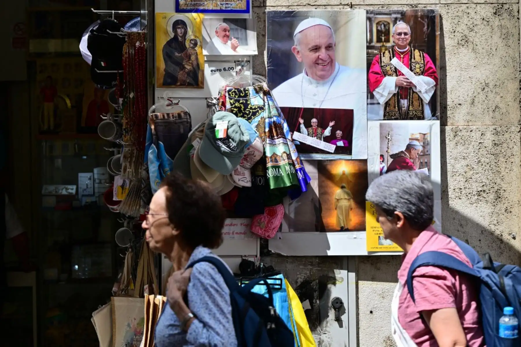 Peatones pasan junto a fotografías del difunto Papa Francisco y del recién elegido Papa León XIV, exhibidas en la fachada de una tienda en Roma, Italia, un día después de su elección. Foto: AFP