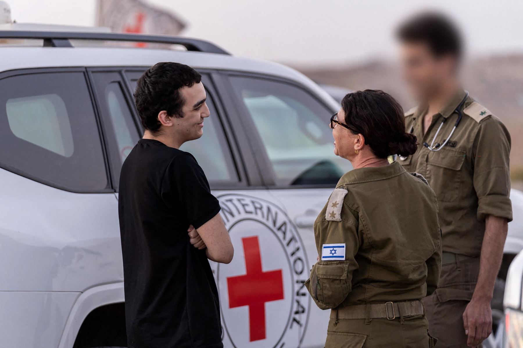 Esta fotografía, difundida por la oficina de prensa del gobierno israelí (OPG), muestra al recién liberado rehén israelí-estadounidense Edan Alexender hablando con soldados israelíes cerca de un vehículo de la Cruz Roja Internacional. Foto: AFP