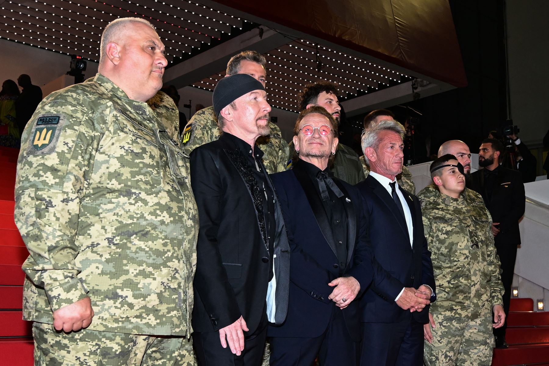 El músico británico-irlandés The Edge, el cantautor y productor ejecutivo irlandés Bono (centro) y el actor, guionista y director de cine estadounidense Sean Penn posan con militares ucranianos a su llegada a la proyección de la película "Bono: Historias de rendición" en la 78.ª edición de Cannes. Foto: ANDINA/ AFP