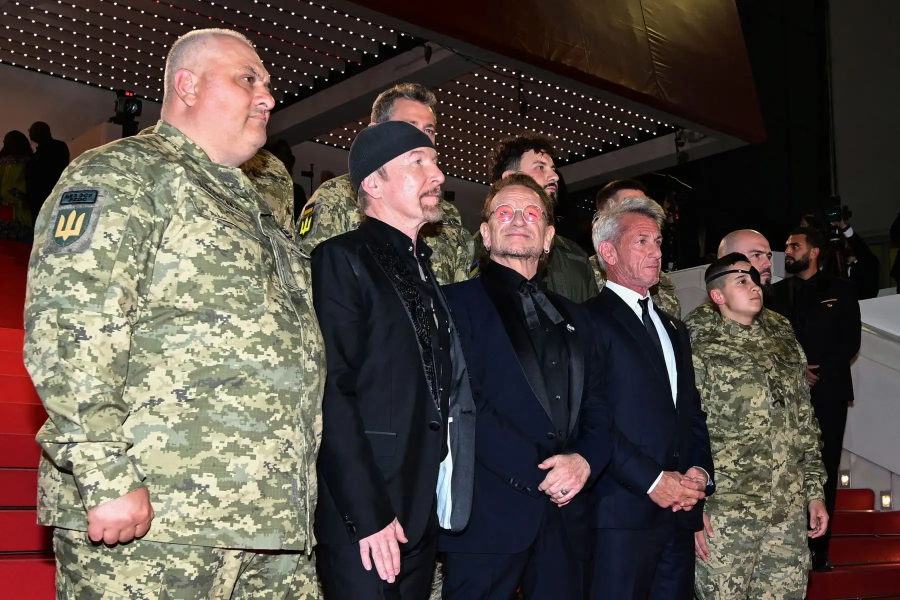 El músico británico-irlandés The Edge, el cantautor y productor ejecutivo irlandés Bono (centro) y el actor, guionista y director de cine estadounidense Sean Penn posan con militares ucranianos a su llegada a la proyección de la película "Bono: Historias de rendición" en la 78.ª edición de Cannes. Foto: ANDINA/ AFP