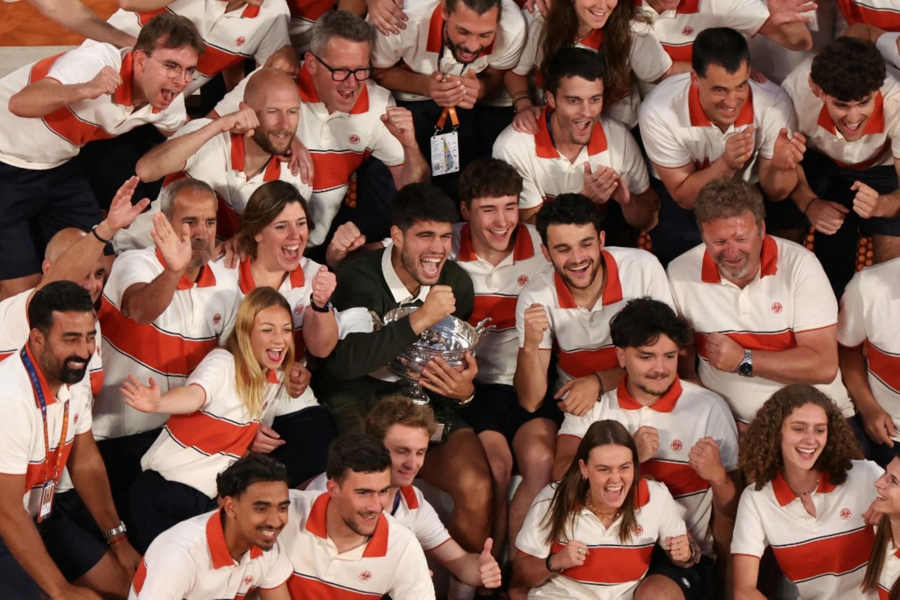 El español Carlos Alcaraz posa con su trofeo entre los miembros del personal de Roland-Garros después de su victoria en el partido de individuales masculinos contra el italiano Jannik Sinner en el día 15 del torneo de tenis del Abierto de Francia en la cancha Suzanne-Lenglen en el Complejo Roland-Garros en París el 8 de junio de 2025. (Foto de ALAIN JOCARD / AFP)