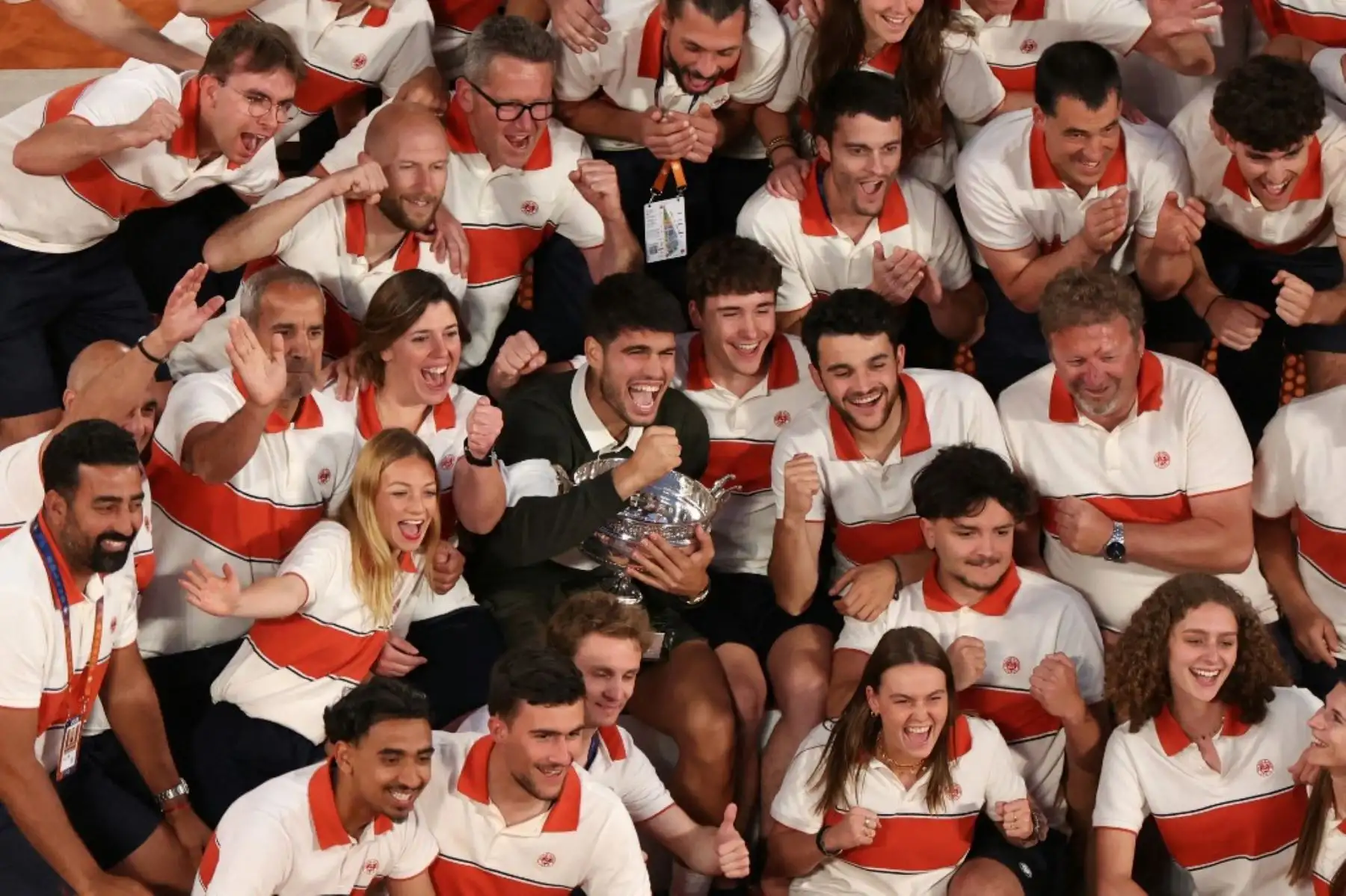 El español Carlos Alcaraz posa con su trofeo entre los miembros del personal de Roland-Garros después de su victoria en el partido de individuales masculinos contra el italiano Jannik Sinner en el día 15 del torneo de tenis del Abierto de Francia en la cancha Suzanne-Lenglen en el Complejo Roland-Garros en París el 8 de junio de 2025. (Foto de ALAIN JOCARD / AFP)