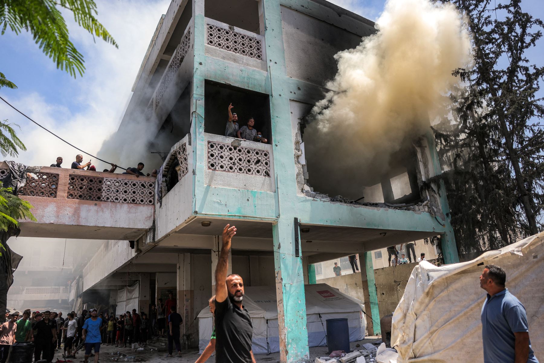 Los hombres gritan a otros abajo mientras se elevan columnas de humo mientras los socorristas intentan extinguir un incendio tras un ataque israelí en la escuela Osama bin Zaid de la UNRWA en el distrito de Saftawi, en el oeste de Jabalia, en el norte de la Franja de Gaza. AFP
