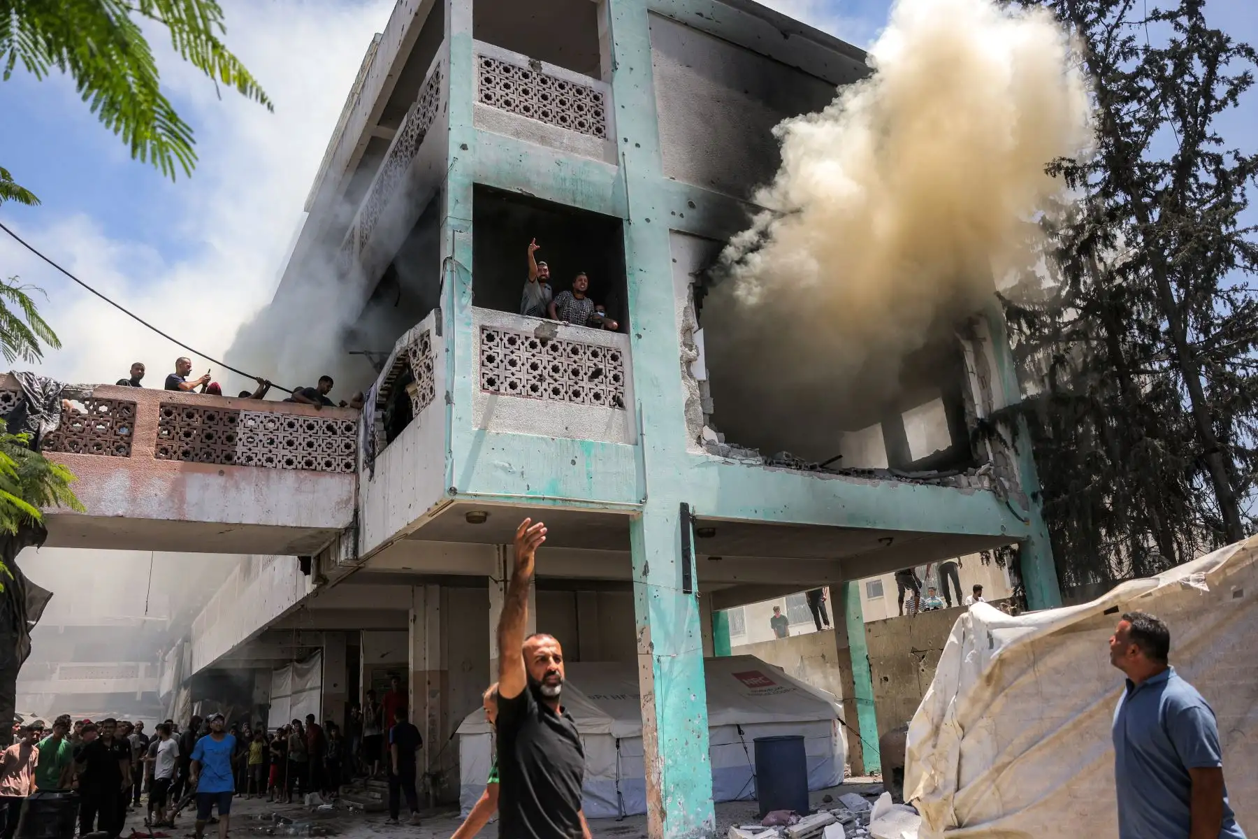 Los hombres gritan a otros abajo mientras se elevan columnas de humo mientras los socorristas intentan extinguir un incendio tras un ataque israelí en la escuela Osama bin Zaid de la UNRWA en el distrito de Saftawi, en el oeste de Jabalia, en el norte de la Franja de Gaza. AFP