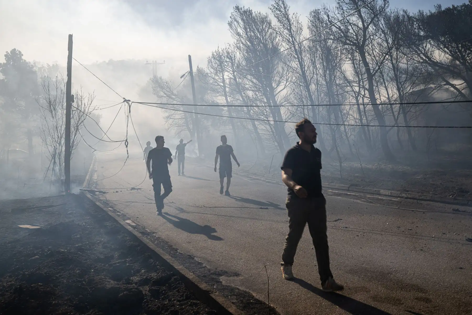Los residentes locales caminan entre el humo a lo largo de una carretera devastada por un incendio forestal en Pikermi, a unos 30 kilómetros al este de Atenas. AFP