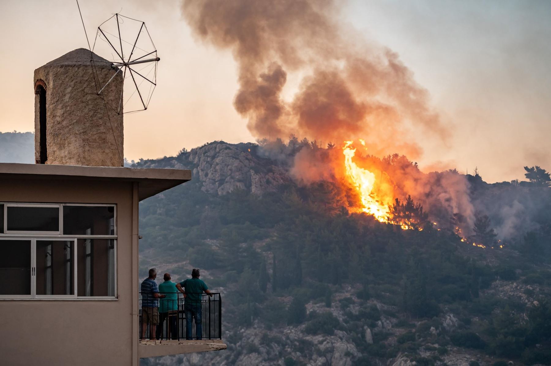 Personas observan cómo un incendio forestal quema tierras forestales en la isla de Quíos, Grecia. AFP