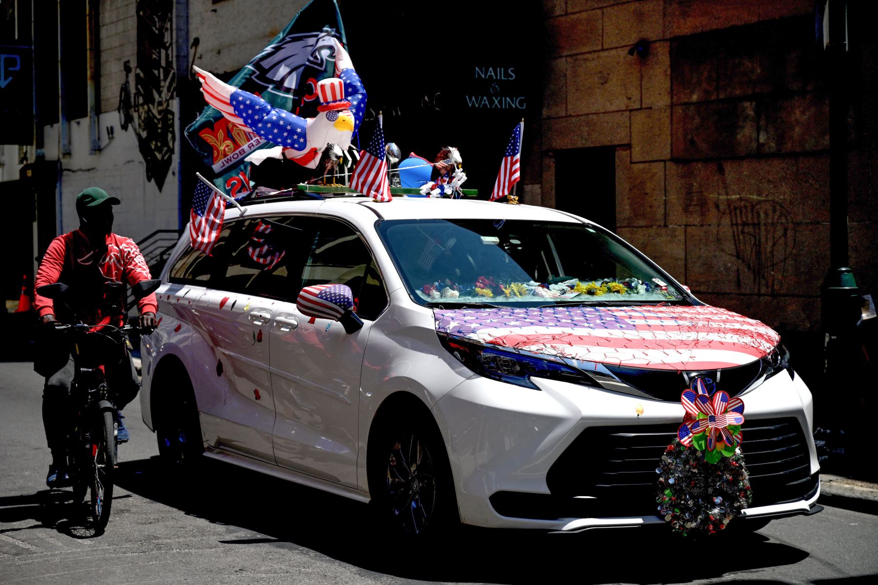 Un hombre monta en bicicleta junto a un automóvil decorado con símbolos nacionales de Estados Unidos durante el Día de la Independencia en Filadelfia, Pensilvania. Foto: AFP