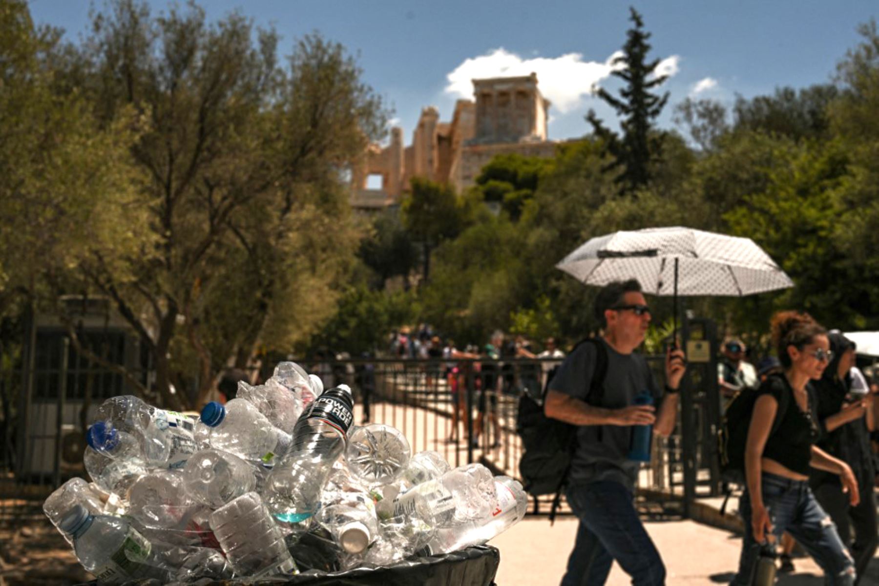 Turistas pasan junto a un contenedor de basura repleto de botellas de plástico cerca de la colina de la Acrópolis en Atenas . El principal monumento arqueológico de Grecia, la Acrópolis, estuvo parcialmente cerrado como parte de las medidas de emergencia para proteger a los visitantes y trabajadores de todo el país durante una ola de calor de cuatro días. 
Foto: AFP