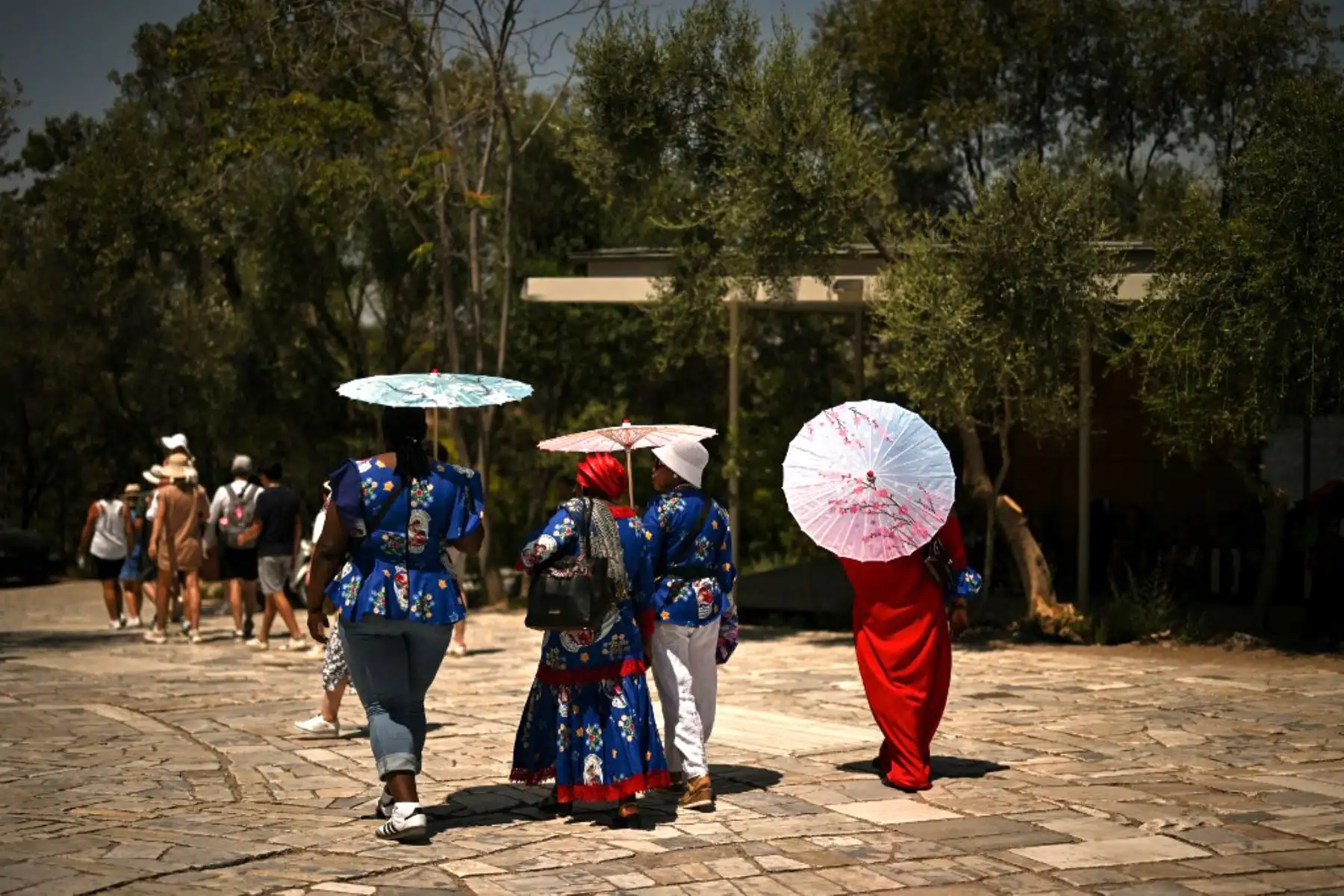 Turistas con paraguas caminan frente a la Acrópolis, la cual permanece cerrada, en Atenas. El principal monumento arqueológico de Grecia, la Acrópolis, permaneció parcialmente cerrado como parte de las medidas de emergencia para proteger a visitantes y trabajadores de todo el país durante una ola de calor de cuatro días. 
Foto: AFP