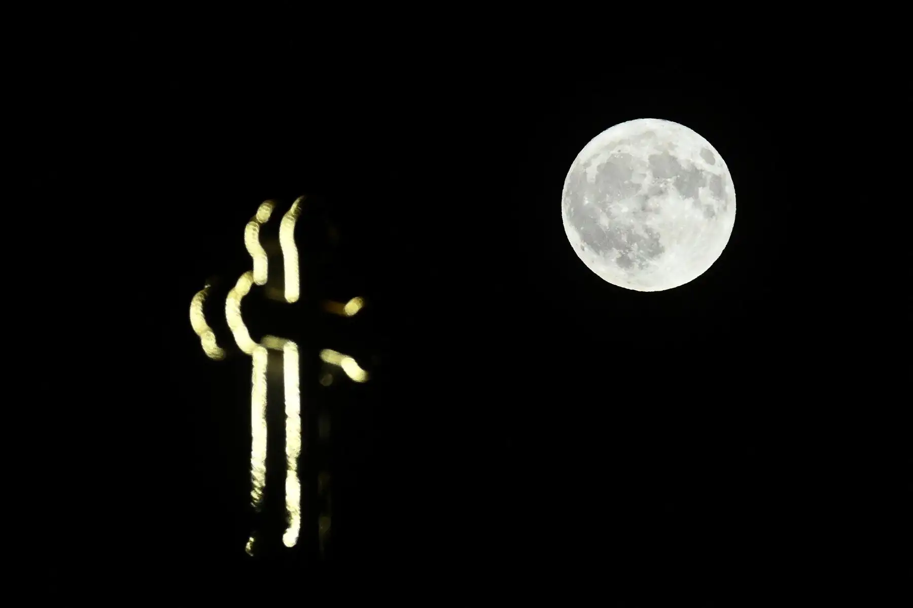 La luna llena sale detrás de una cruz en Skopje. AFP