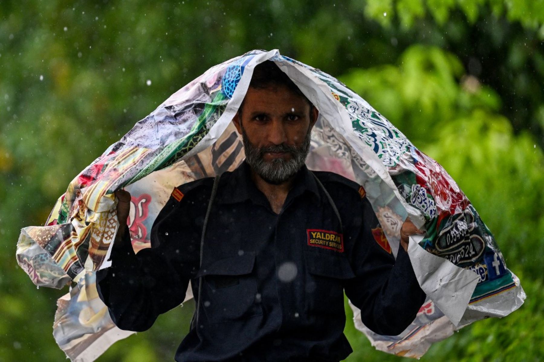 Un hombre usa una sábana de plástico para cubrirse durante las lluvias monzónicas en Islamabad. AFP