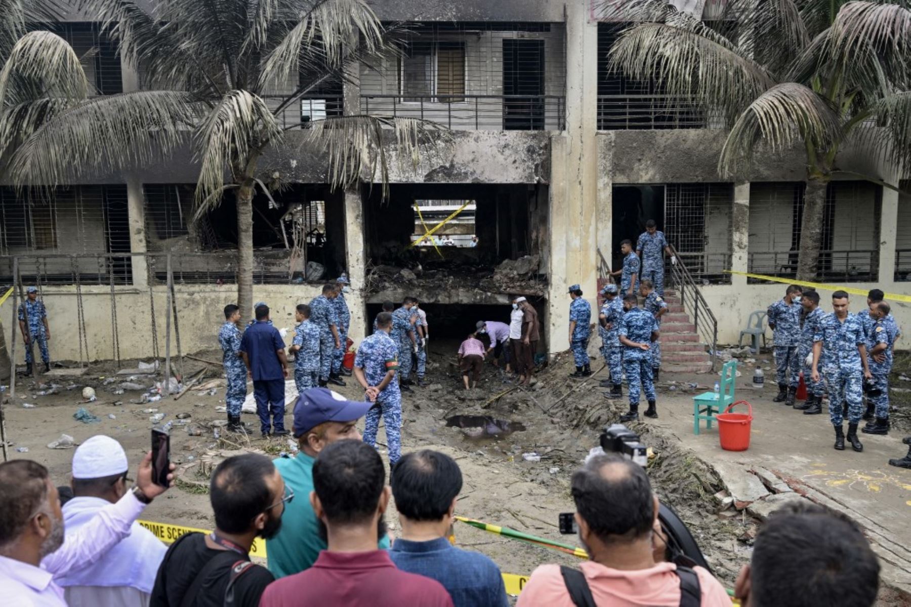 Los espectadores se reunieron mientras el personal de la Fuerza Aérea de Bangladesh inspeccionaba el lugar del accidente un día después de que un avión de entrenamiento se estrellara contra una escuela en Dhaka. AFP