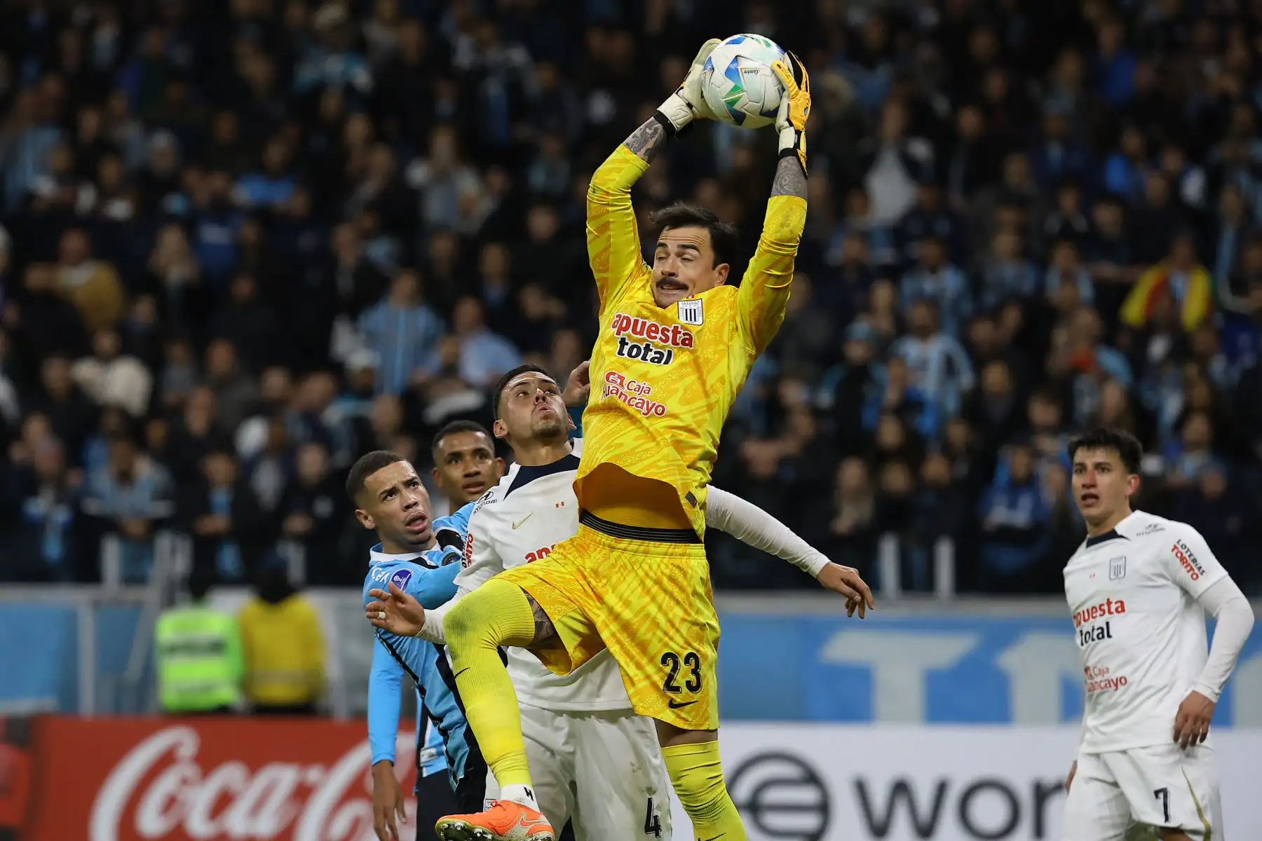 El portero boliviano de Alianza Lima, Guillermo Viscarra, atrapa el balón superando a su compañero defensor Erick Noriega y al delantero de Gremio, Alysson, durante el partido de eliminatoria de la Copa Sudamericana entre Gremio de Brasil y Alianza Lima de Perú en el estadio Arena do Gremio en Porto Alegre. Foto: ANDINA/AFP