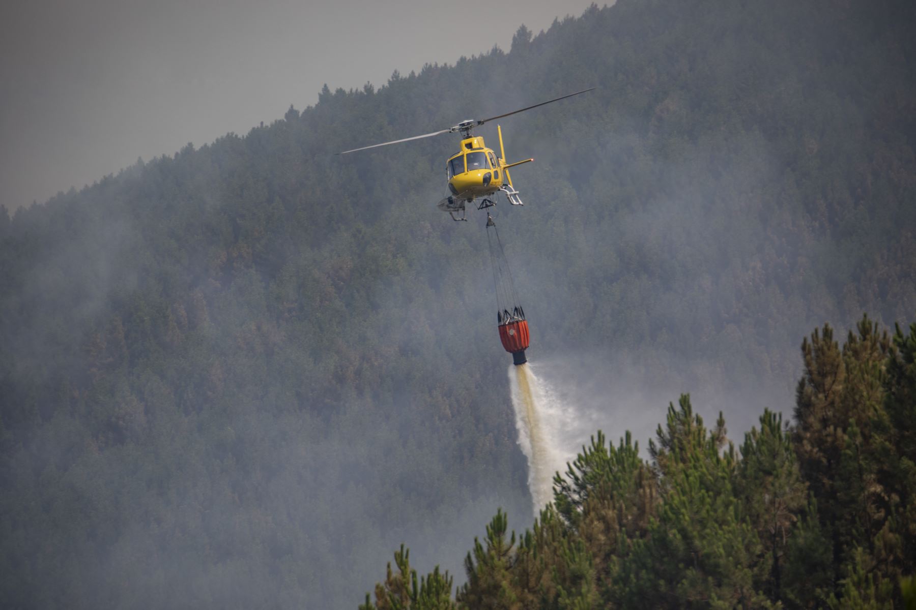Un helicóptero de bomberos arroja agua mientras los bomberos en tierra luchan contra un incendio forestal cerca de Caminomorisco, en la provincia occidental española de Cáceres. AFP