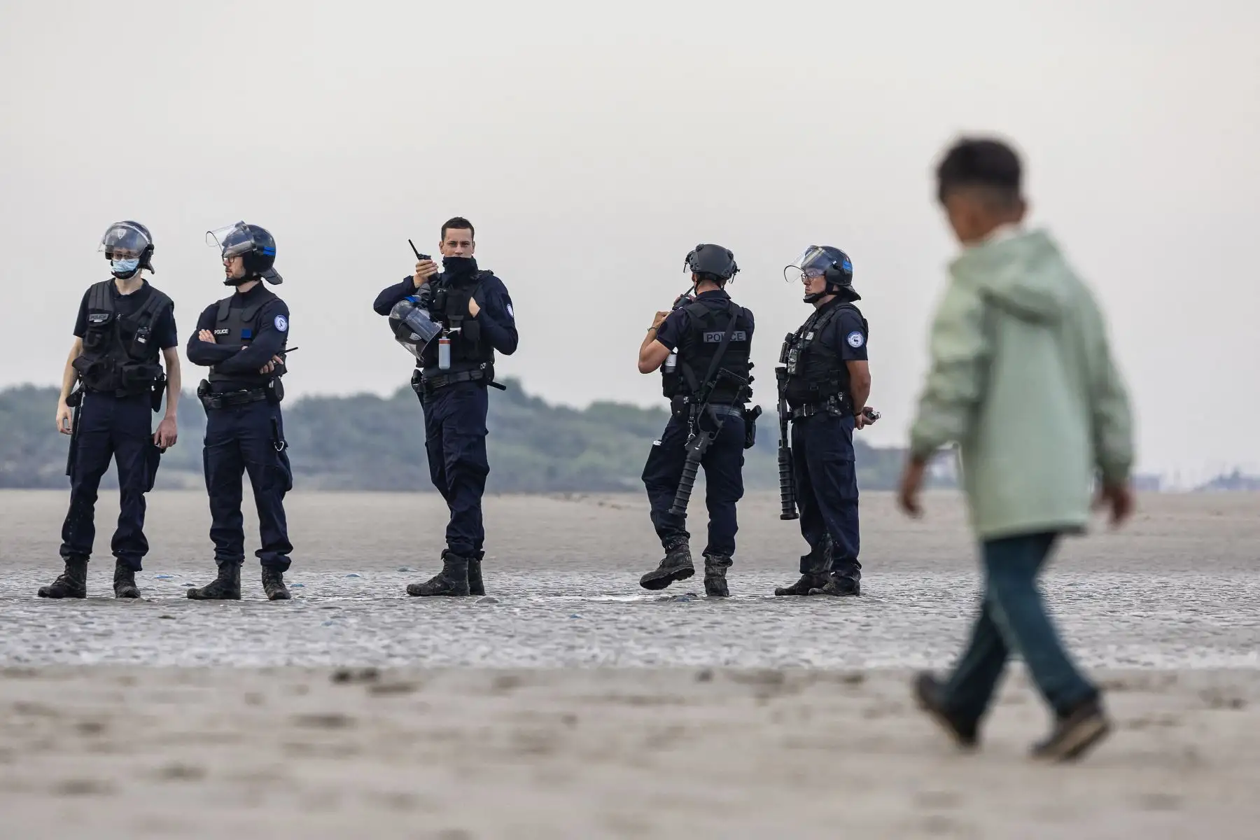 Agentes de la policía francesa observan a los migrantes caminando de regreso después de no poder abordar un barco de contrabandistas en un intento de cruzar el Canal de la Mancha frente a la playa de Gravelines, en el norte de Francia. AFP