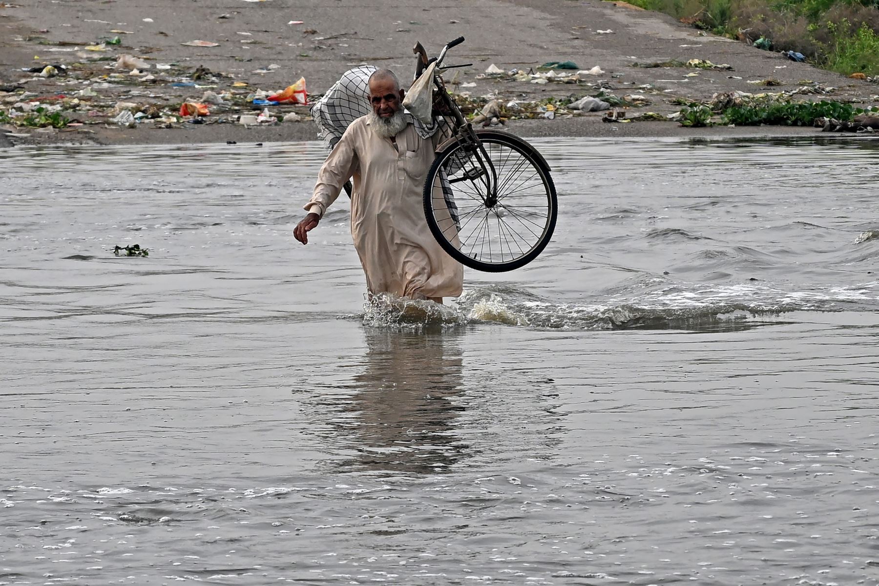 Un hombre lleva su bicicleta mientras camina por una carretera inundada después de las fuertes lluvias monzónicas en Karachi. AFP