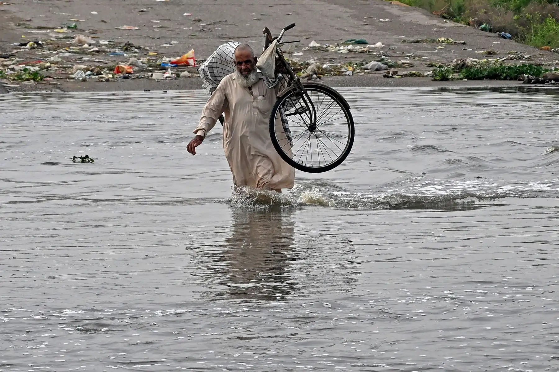 Un hombre lleva su bicicleta mientras camina por una carretera inundada después de las fuertes lluvias monzónicas en Karachi. AFP